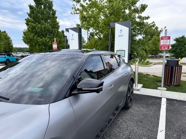 Kia EV6 charging at an Electrify America station with green trees in the background.