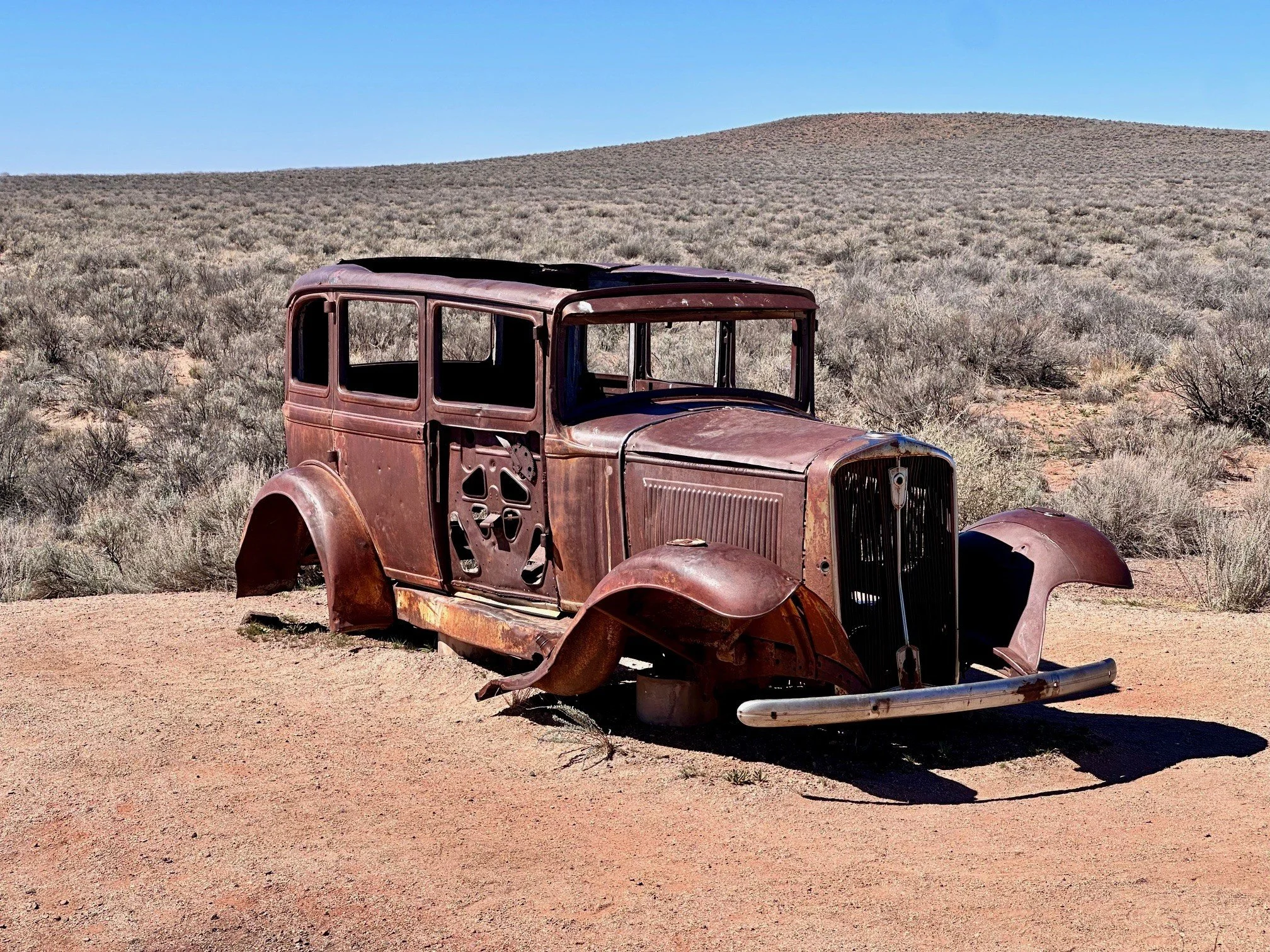 A rusted 1932 Studebaker resting along the old Route 66 alignment in Petrified Forest National Park, a quiet reminder of early road‑trippers crossing the desert long before EVs.