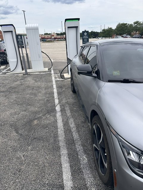 Kia EV6 electric vehicle plugged into Rivian Adventure Network fast charger in Bloomington Illinois parking area.