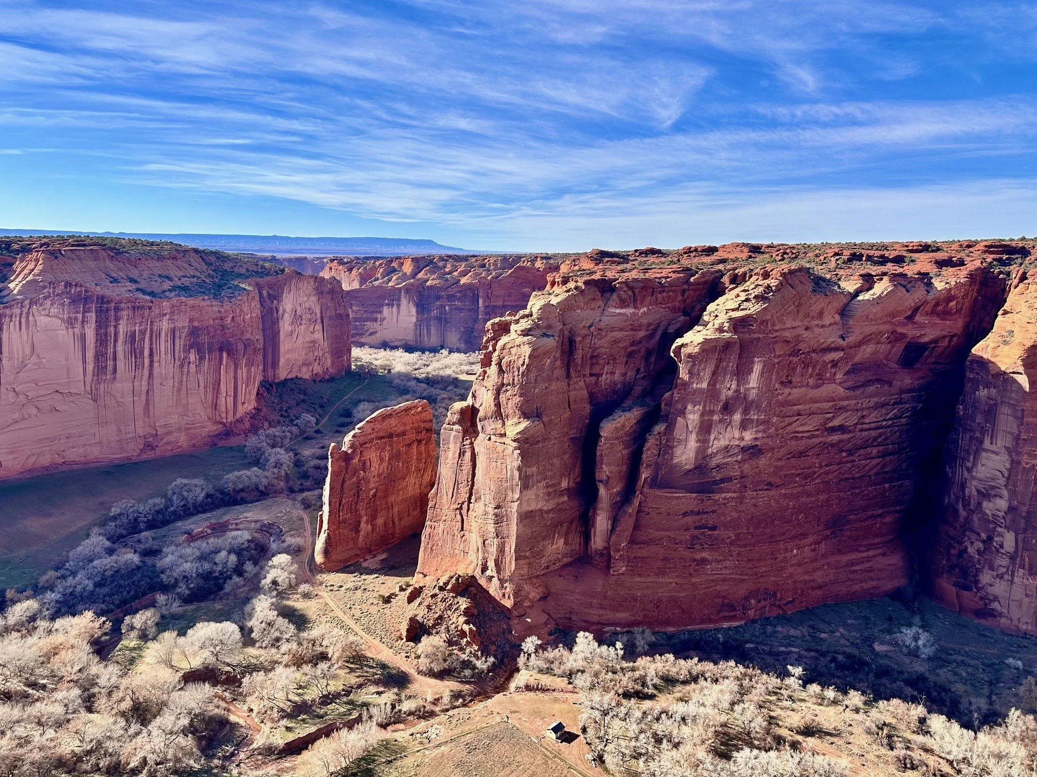 View from Sliding House Overlook at Canyon de Chelly National Monument, with towering red sandstone cliffs, rugged canyon walls, and green vegetation along the canyon floor.