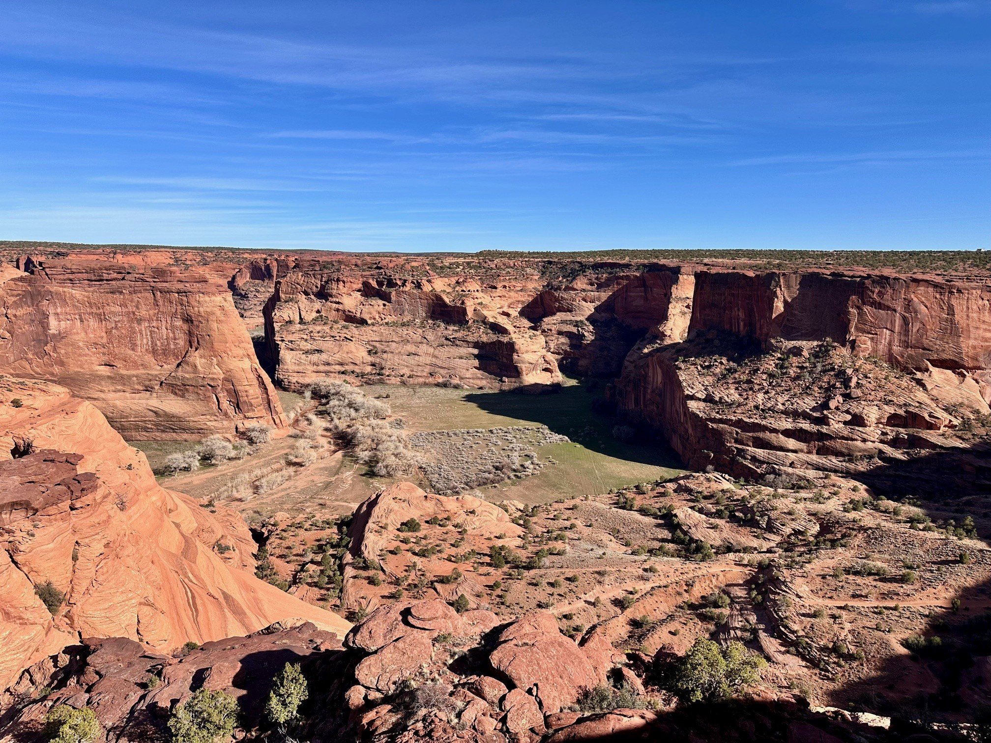 View from Tsegi Overlook at Canyon de Chelly National Monument, with steep red canyon walls, green vegetation, and farmland along the canyon floor.