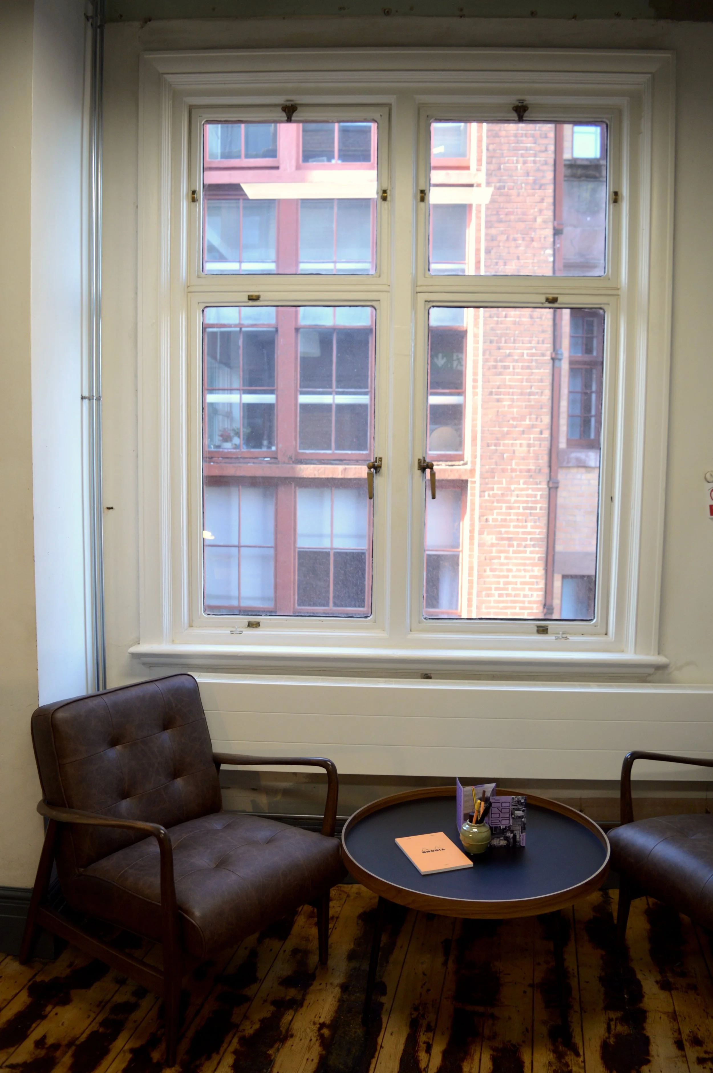 A view of Manchester's red brick architecture from the window of a private studio in SEESAW, with leather chairs seated in front.