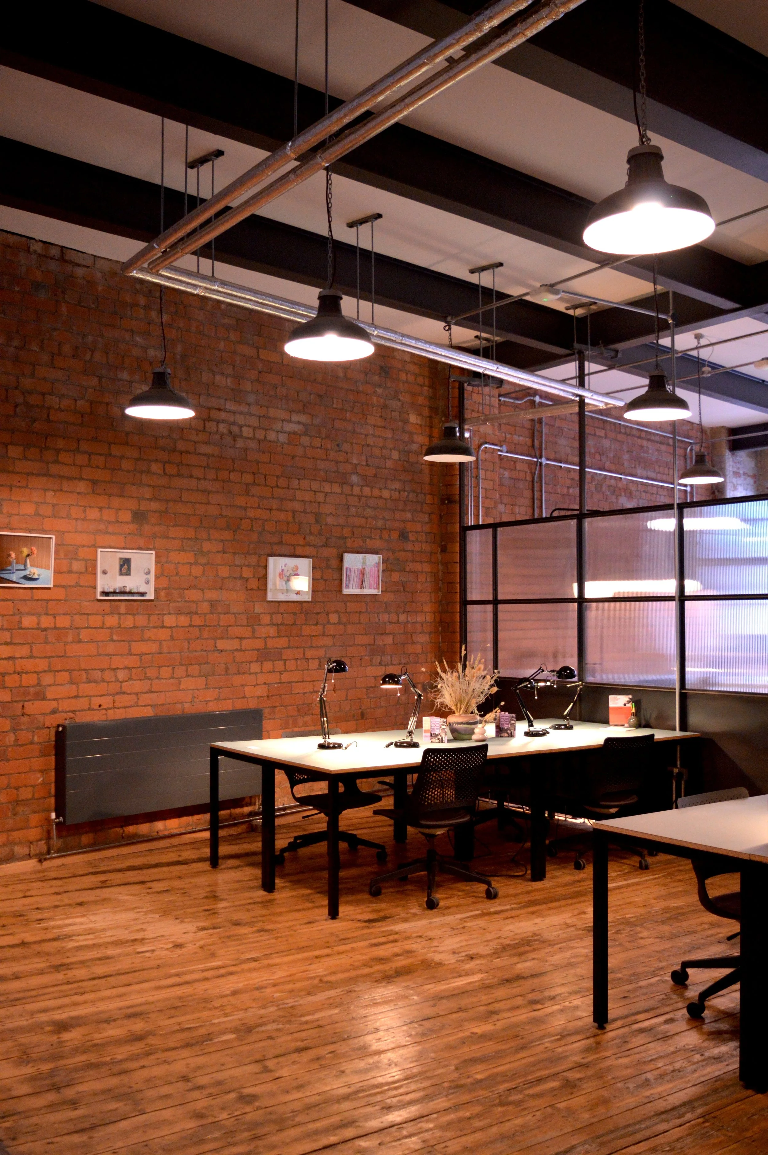 A large partitioned studio space in SEESAW, featuring two desks, wooden floors and red brick walls.