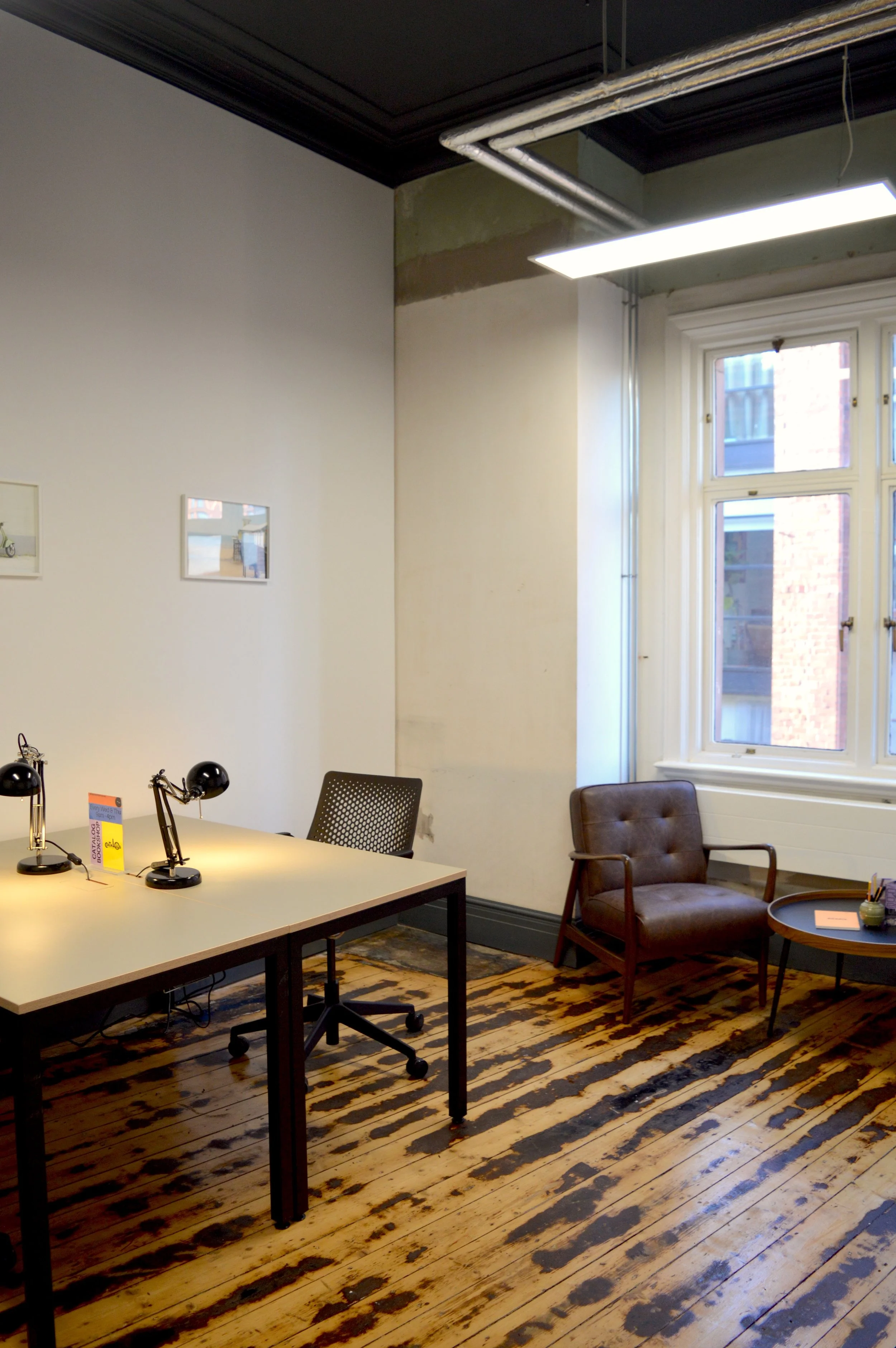 A private studio in SEESAW, featuring a desk, original wooden floors, a leather chair and a view of Manchester from the window.