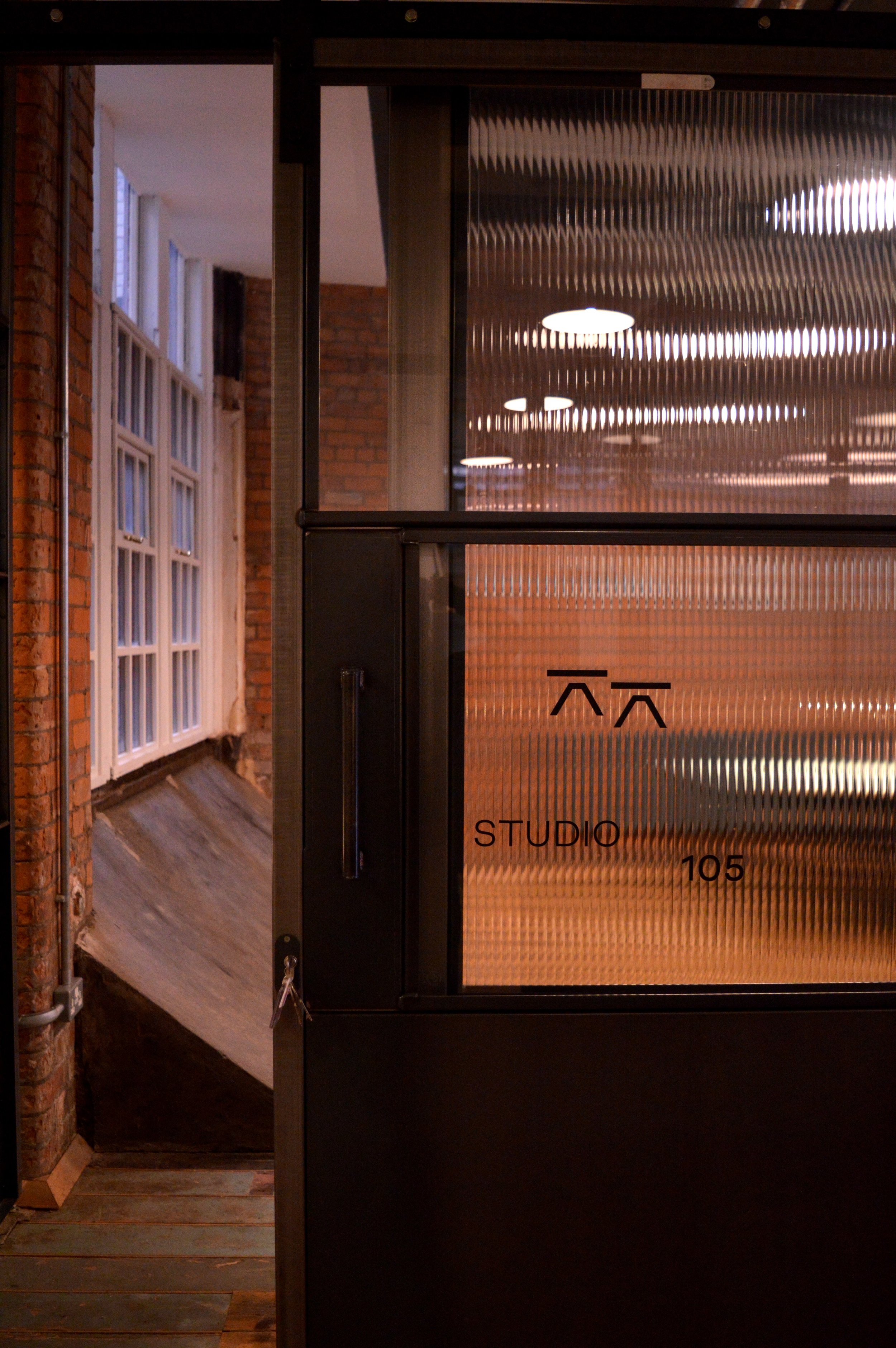 A sliding door opening to Studio 105, a partitioned studio space in SEESAW, a red brick office building in Manchester.