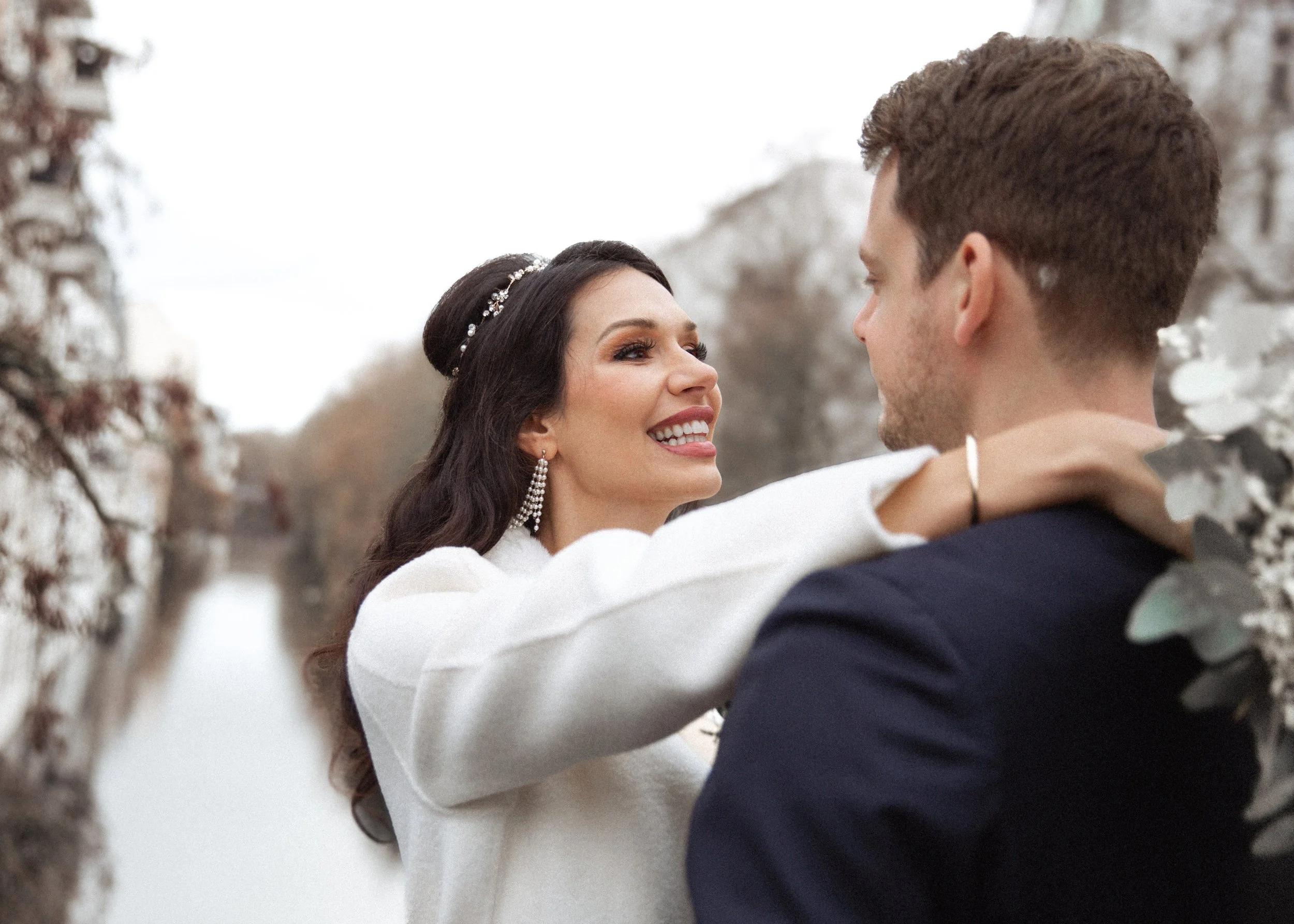 Ein Brautpaar küssen sich draußen im Herbst, die Braut trägt ein weißes Kleid und Schmuck, der Bräutigam trägt einen dunklen Anzug.