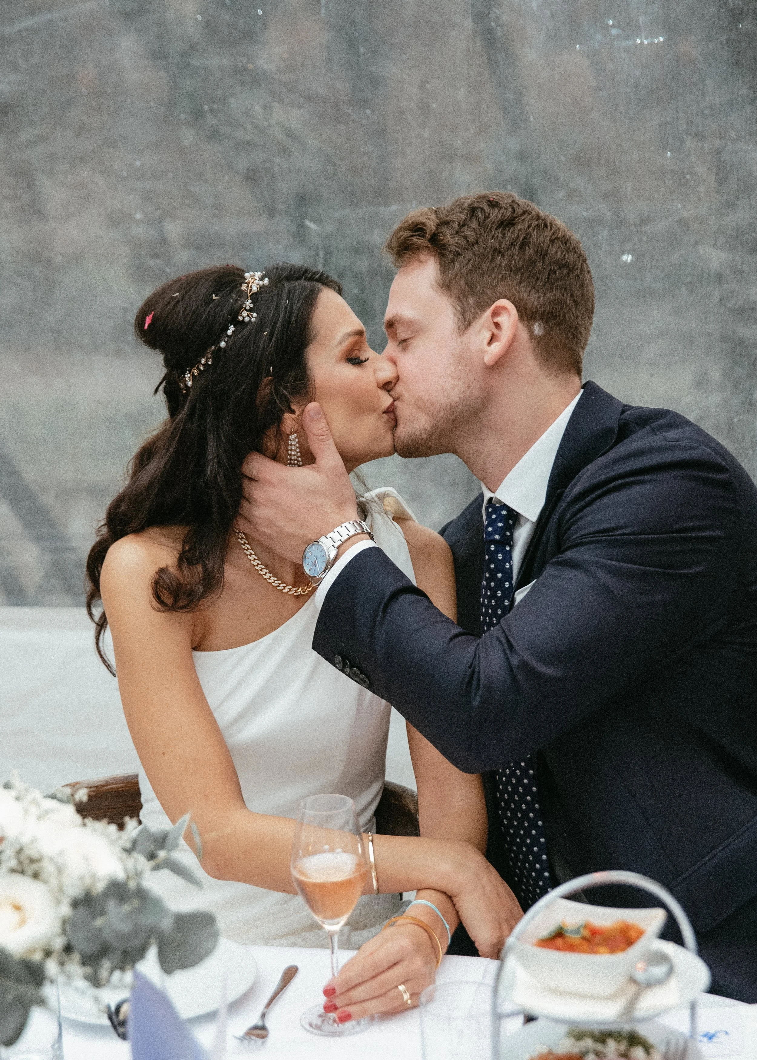 Ein verliebtes Paar bei einer Hochzeit, das sich küsst, während sie an einem Hochzeitstisch sitzen.