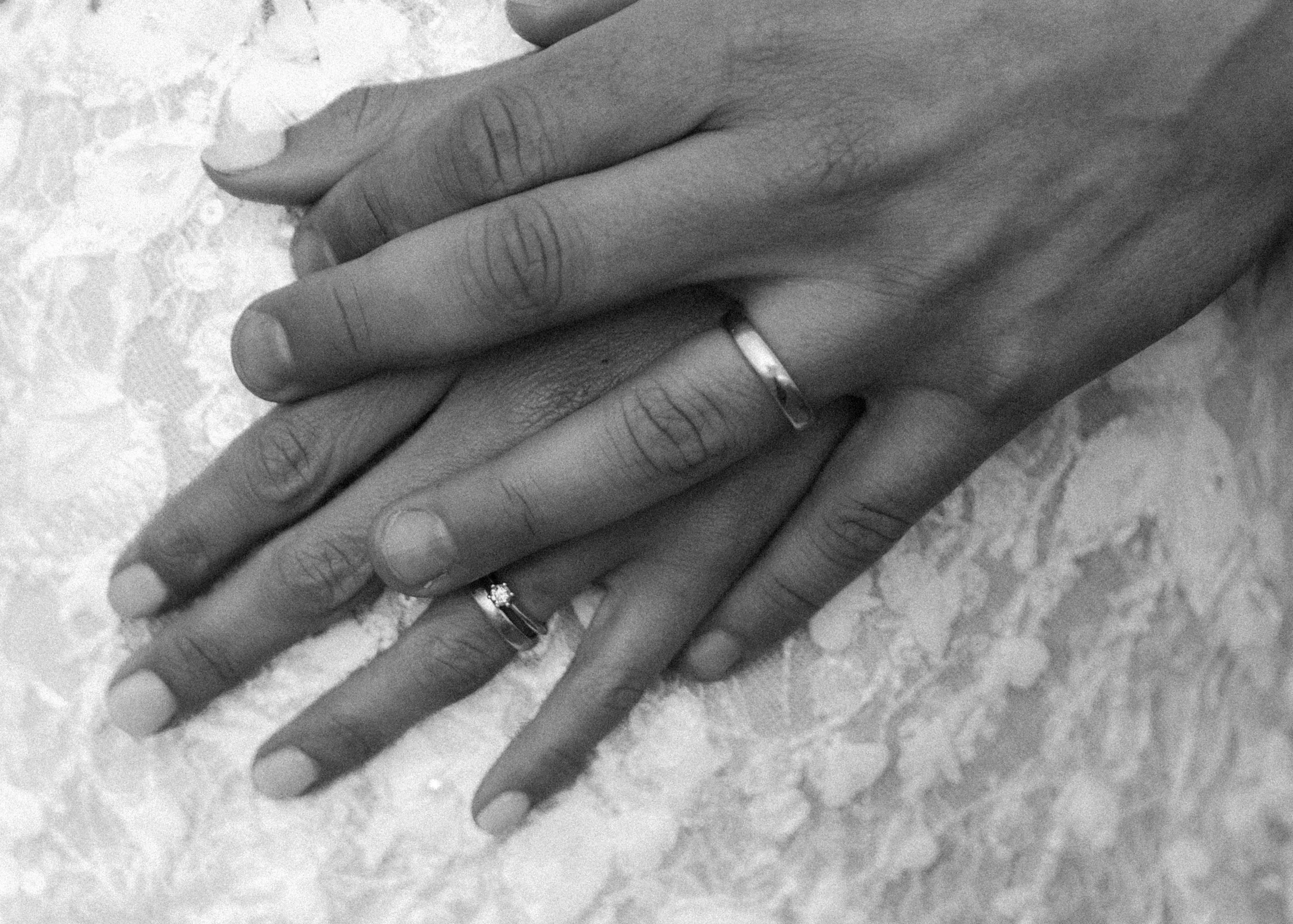 Zwei Hände mit Ringen liegen auf einer Stofffläche, eine Hand liegt auf der anderen.
