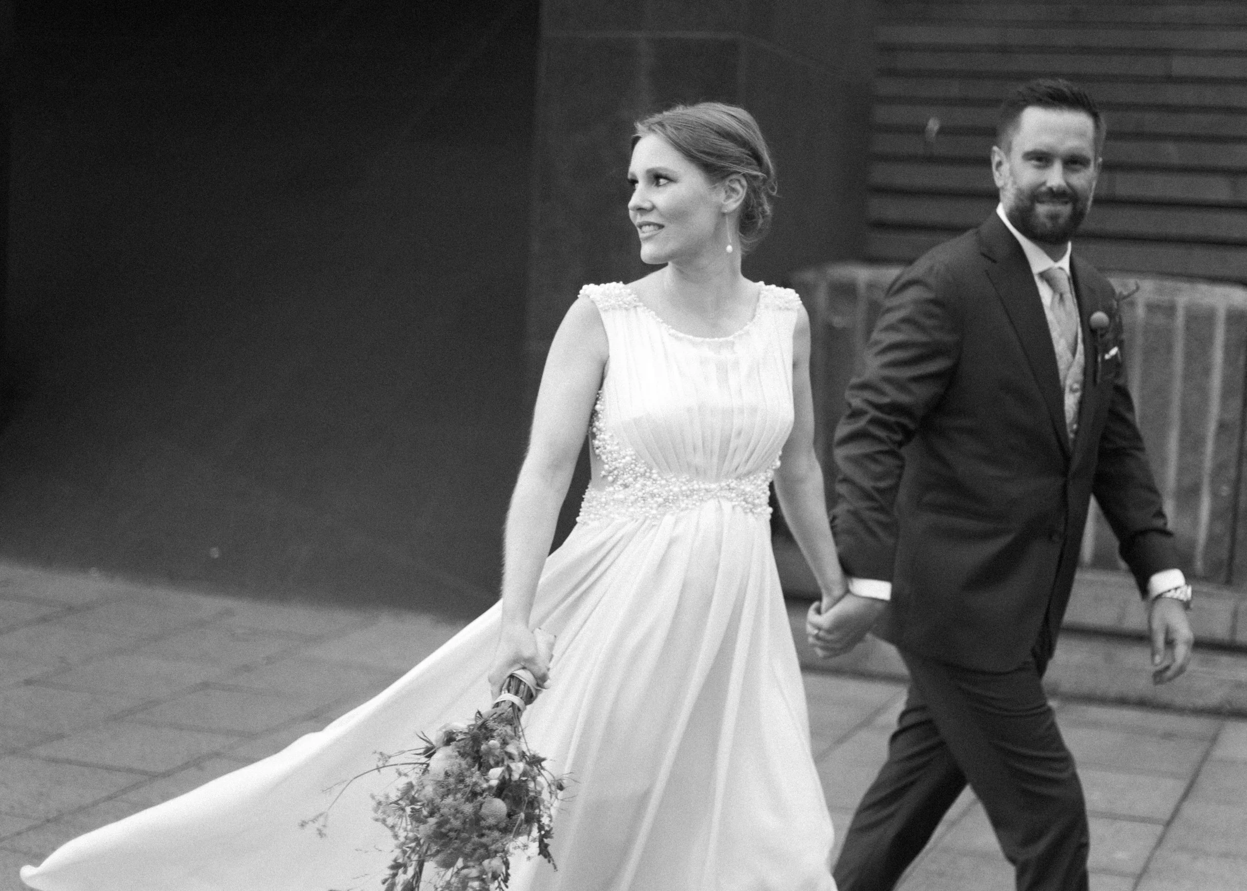 Ein Brautpaar in formeller Kleidung bei ihrer Trauung, die Braut in einem weißen Kleid mit Schleier und das Paar hält Händchen.