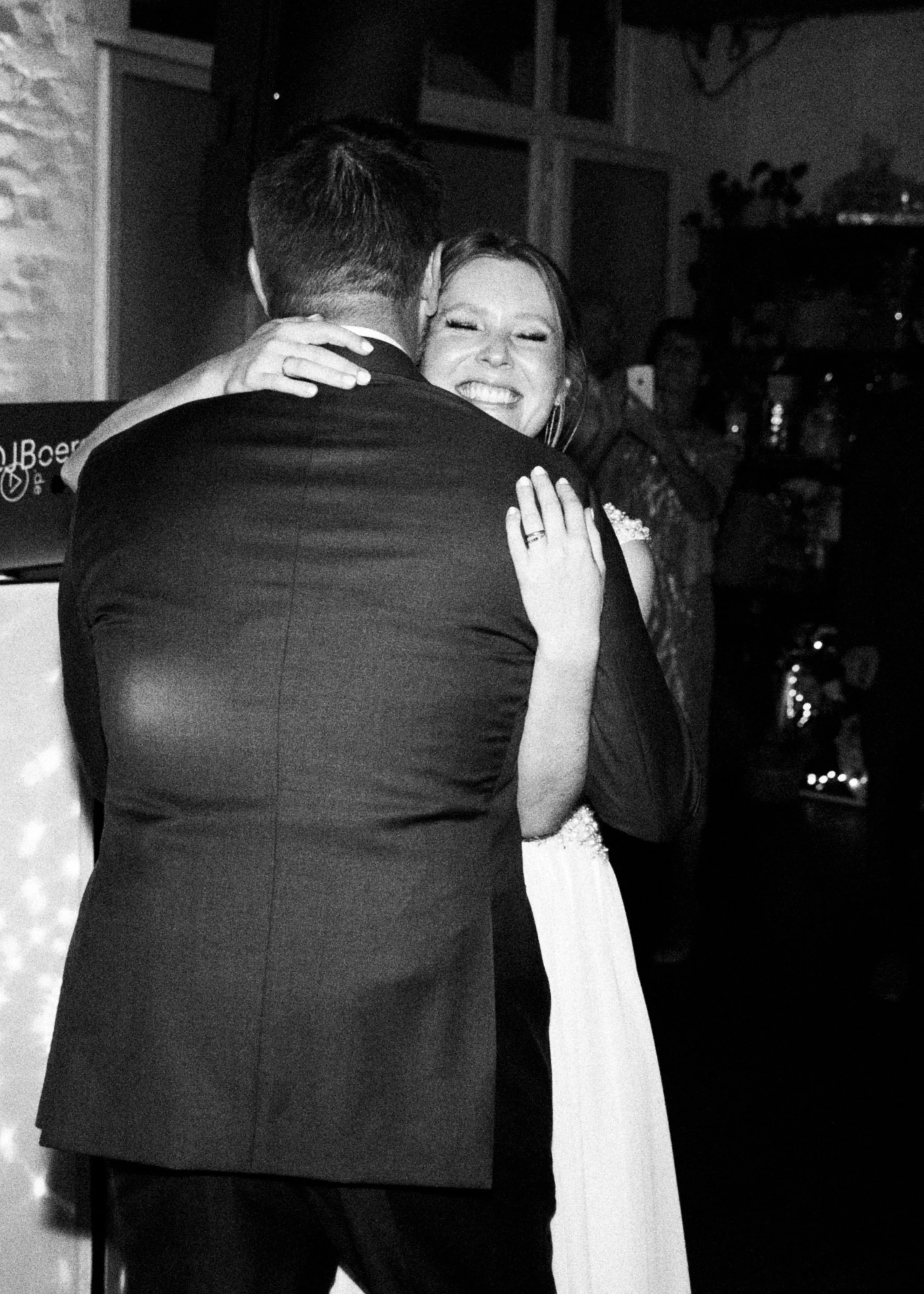 Ein Mann und eine Frau umarmen sich bei einer Feier, die Frau lächelt glücklich.