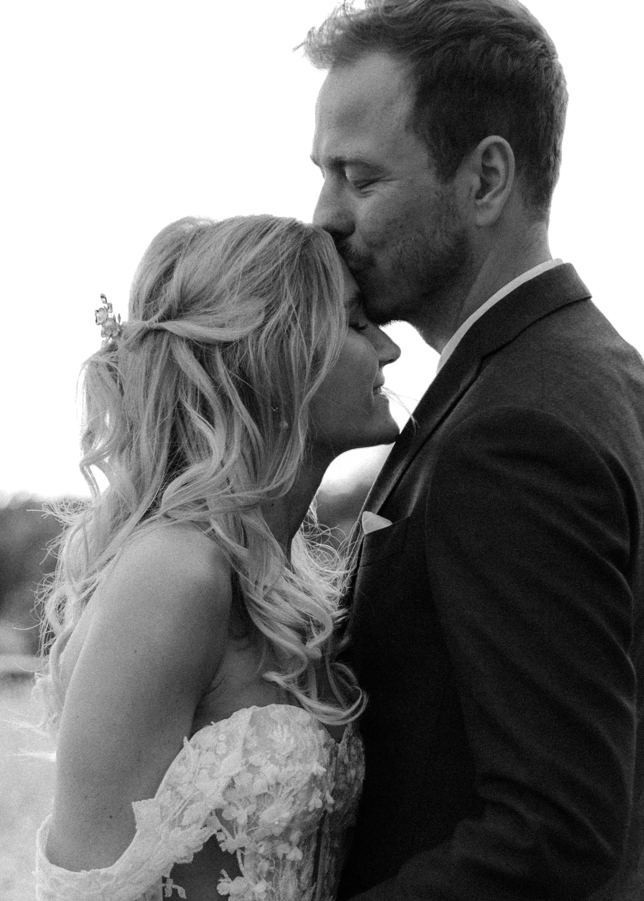 Ein Brautpaar in einer Umarmung, beim Kerzen löschen. Sie trägt ein Hochzeitskleid, er einen Anzug. Schwarz-Weiß-Foto.