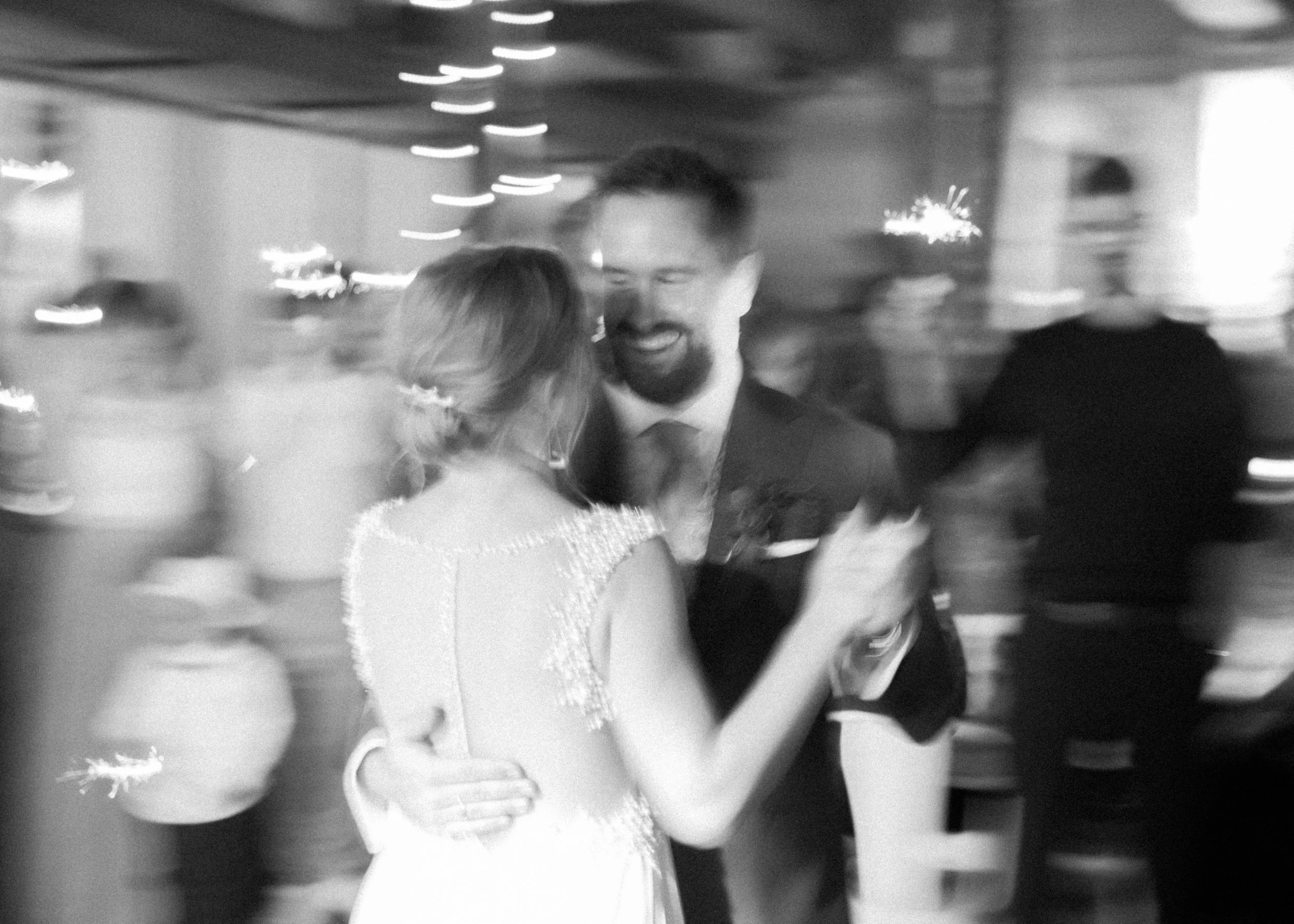 Paar beim Tanzen auf einer Feier, lächelnd, im Schwarz-Weiß, mit unscharfem Hintergrund.