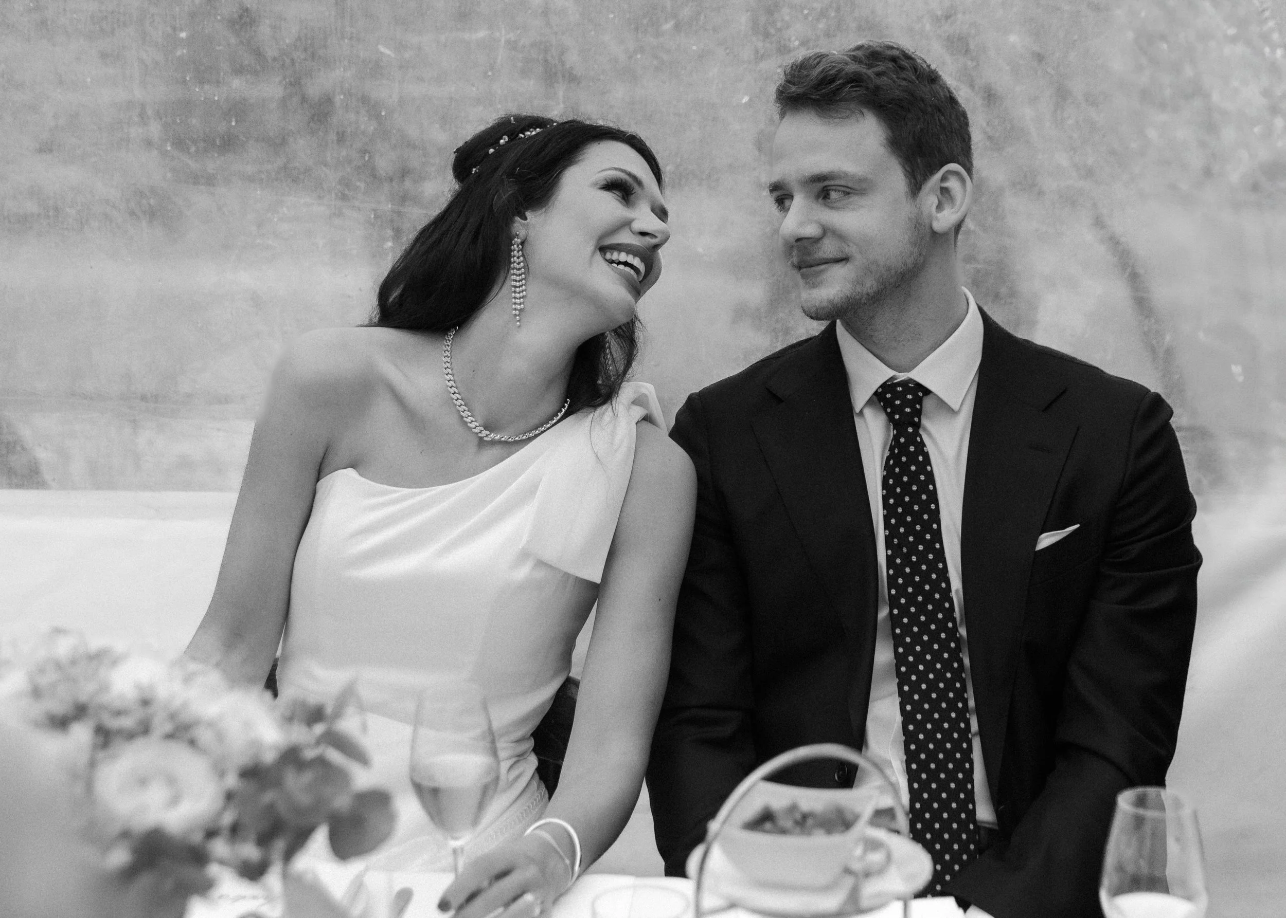 Ein glückliches Paar bei einer formellen Veranstaltung, vermutlich eine Hochzeit, lächelnd und sich anschaulich unterhaltend.