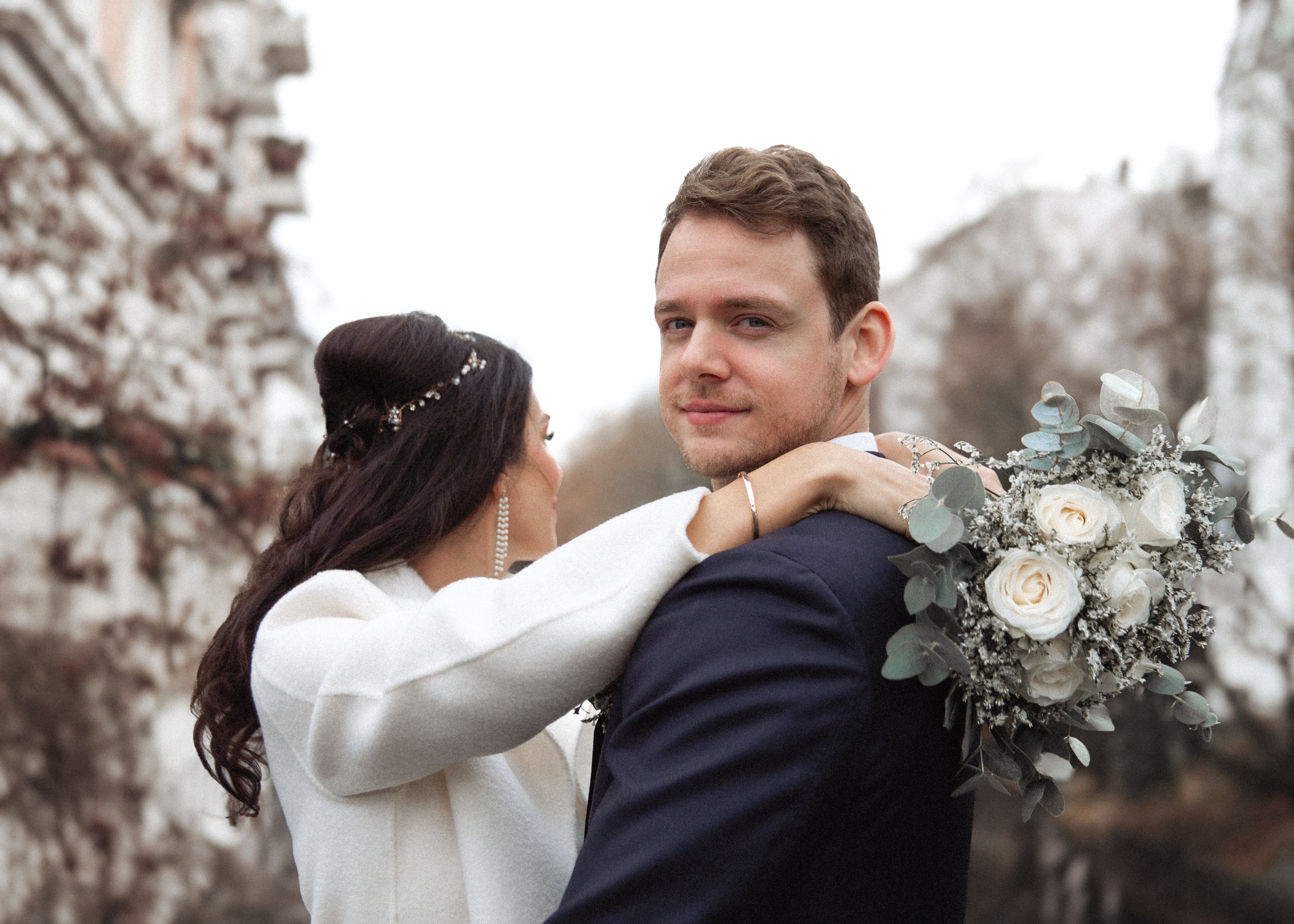 Ein Paar bei einer Hochzeit im Freien, das Braut trägt ein weißes Kleid und der Bräutigam einen dunklen Anzug, mit einem Blumenstrauß in der Hand.