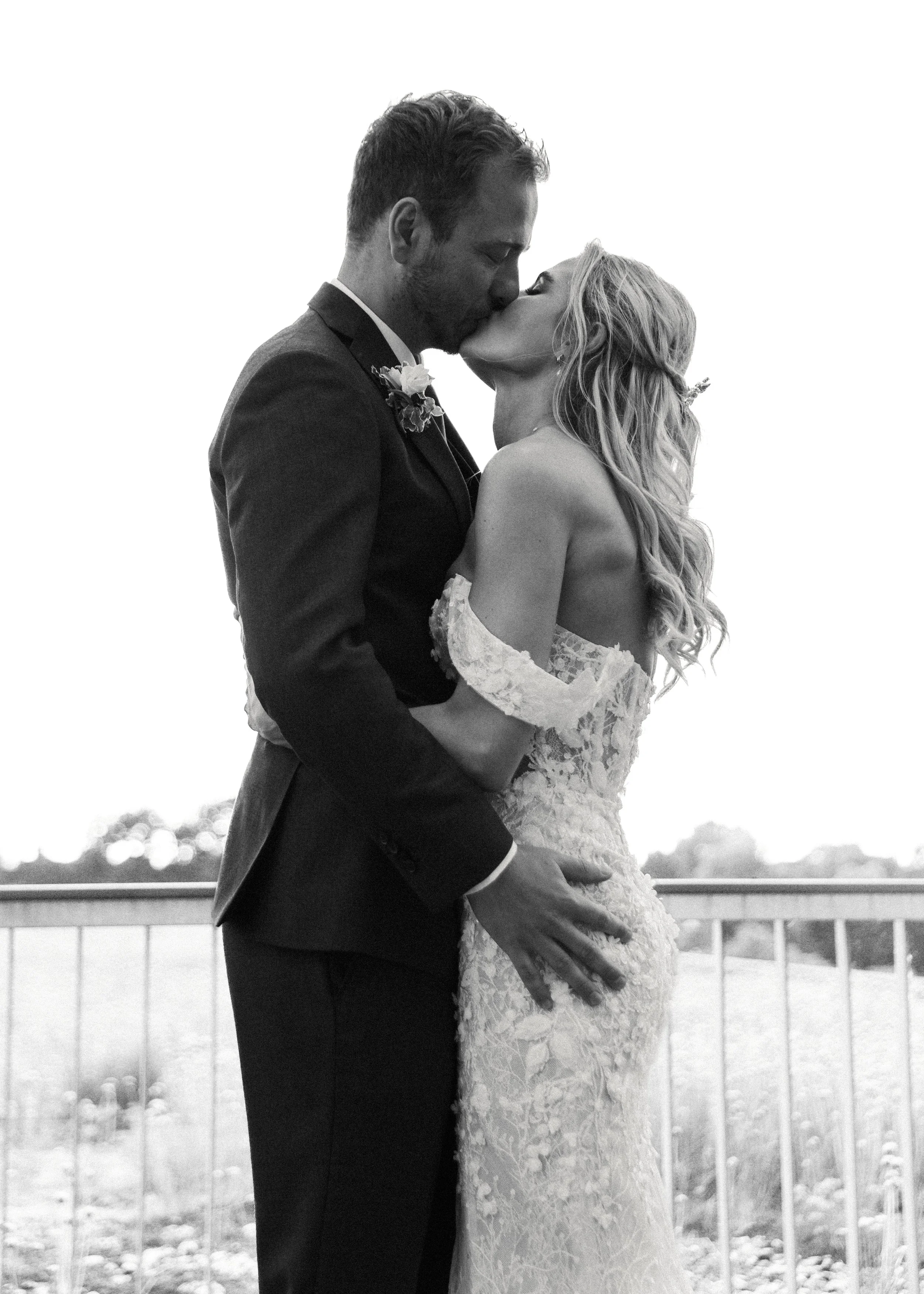 Ein Paar in formeller Kleidung, offenbar auf einer Hochzeit, küsst sich liebevoll.