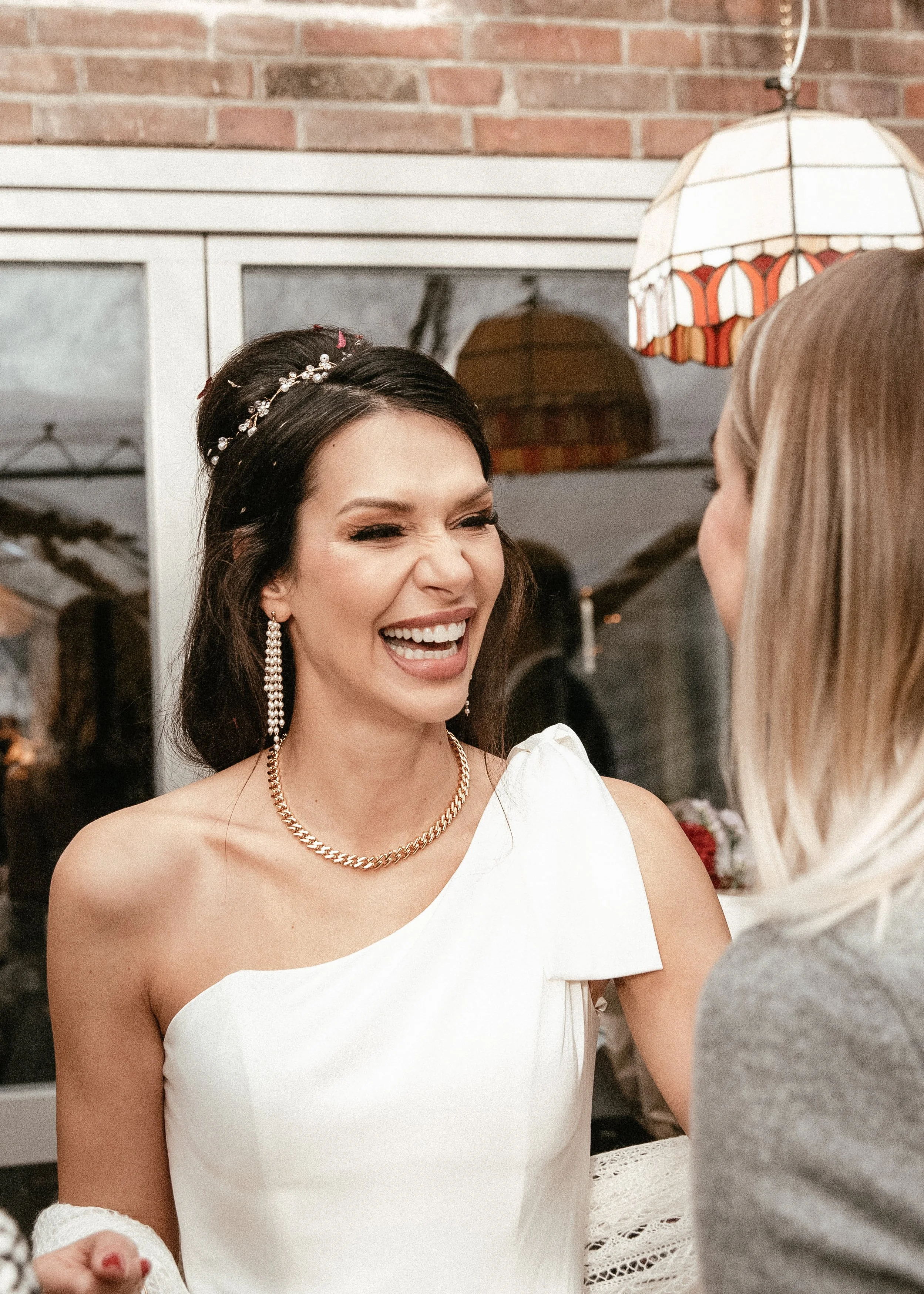 Frau in Hochzeitskleid lacht mit einer anderen Person bei einer Hochzeit.