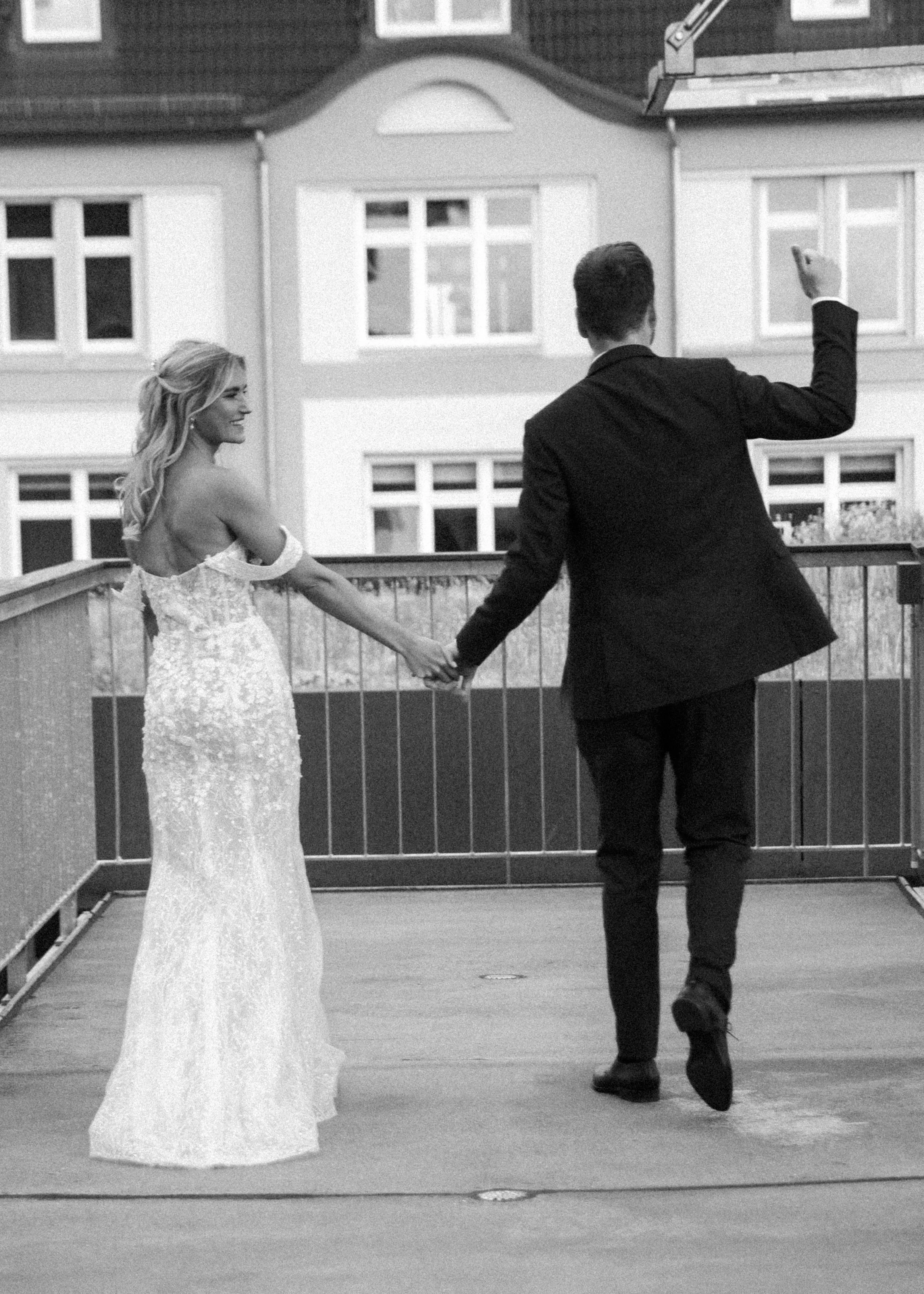 Braut und Bräutigam auf der Hochzeitsfeier, Hand in Hand auf einem Balkon, während der Bräutigam ein Foto macht.