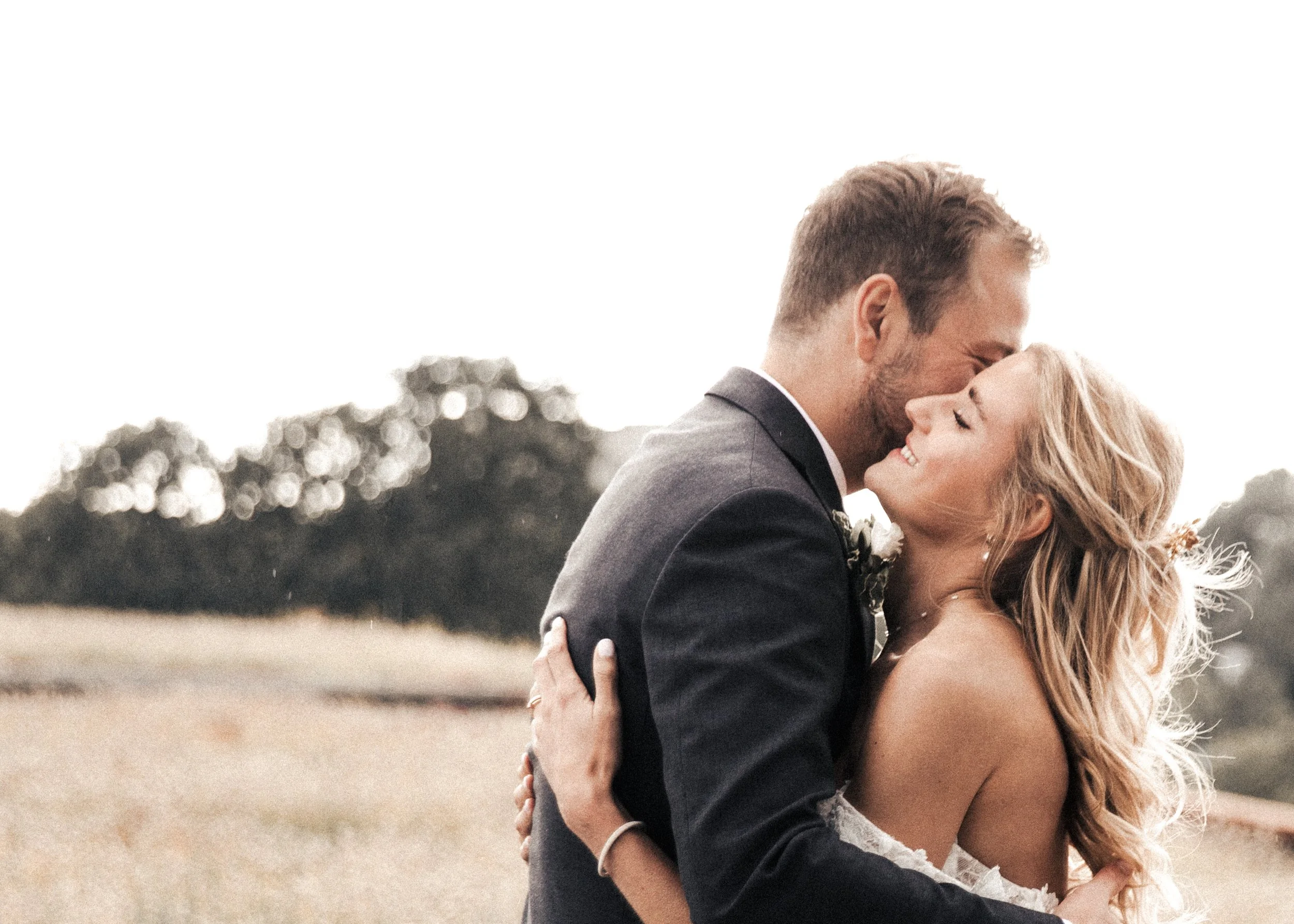 Ein lachendes, verliebtes Paar in formeller Kleidung, das sich in einem Freien umarmt und küsst.