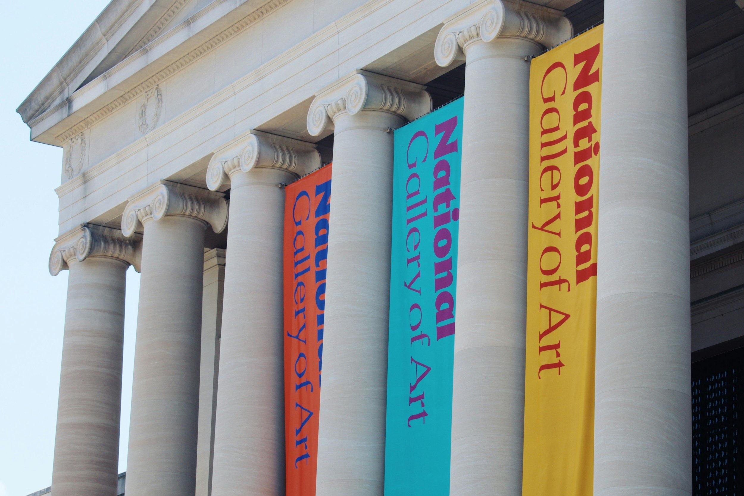 Ancient Greek style building with large white columns and colorful banners hanging between them, featuring text.