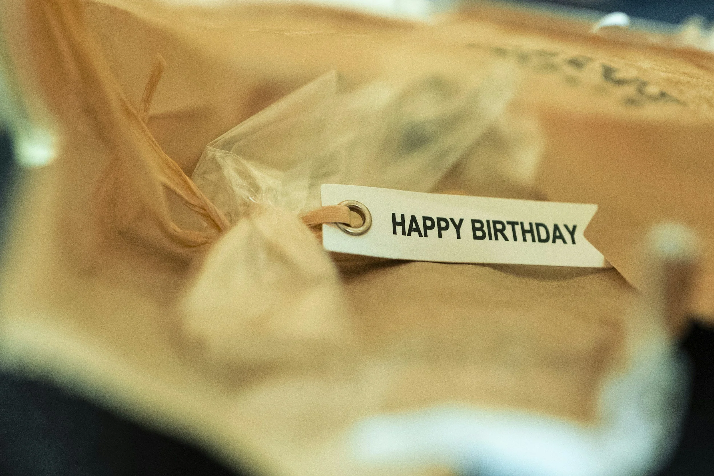 A close-up of a gift bag with a white tag that says 'HAPPY BIRTHDAY' inside. The image is blurry and taken from an unusual angle.