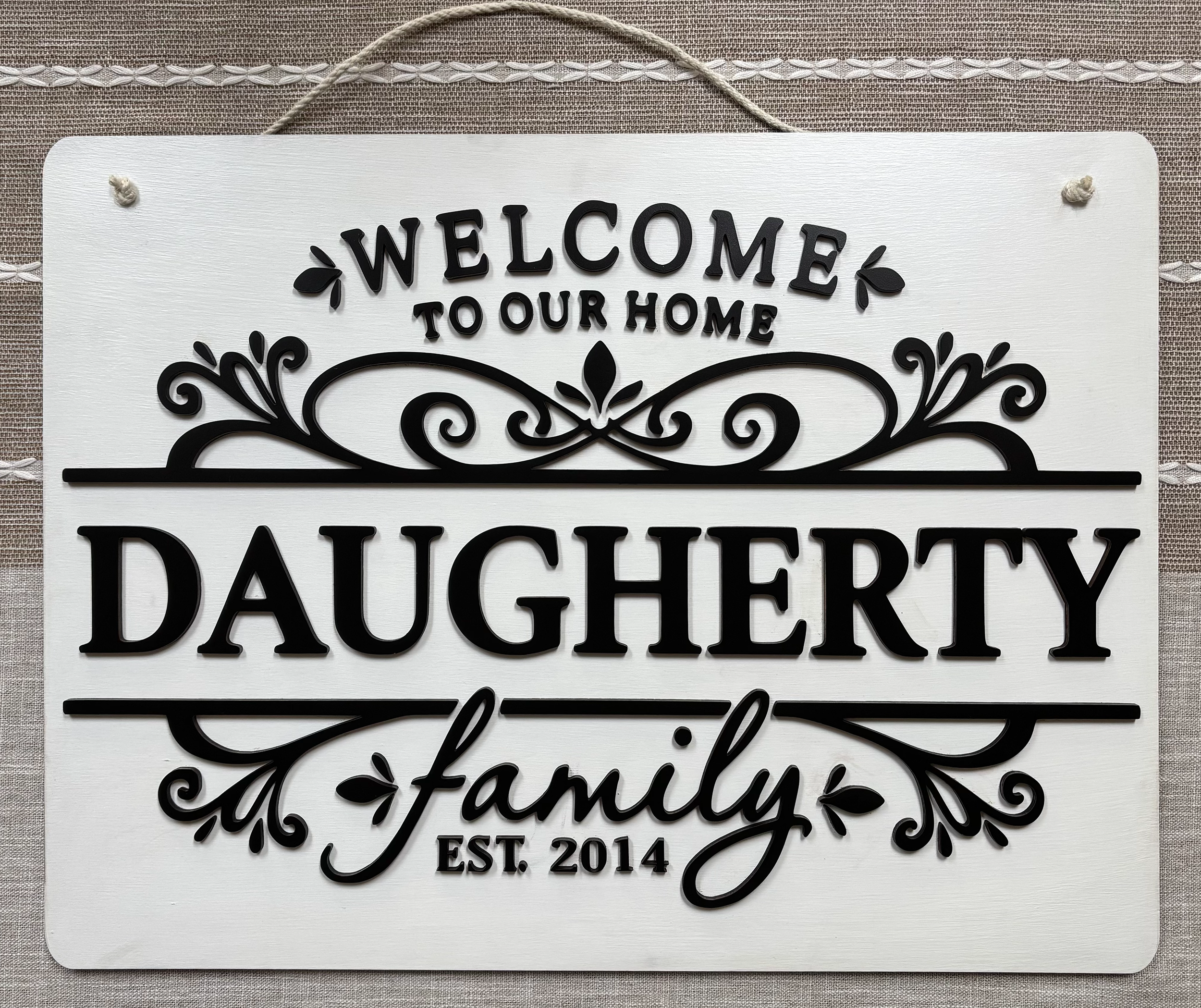 Black and white decorative sign that reads 'Welcome to our home' with stylized floral accents and the words 'Daughter' and 'Foster' partially visible beneath.