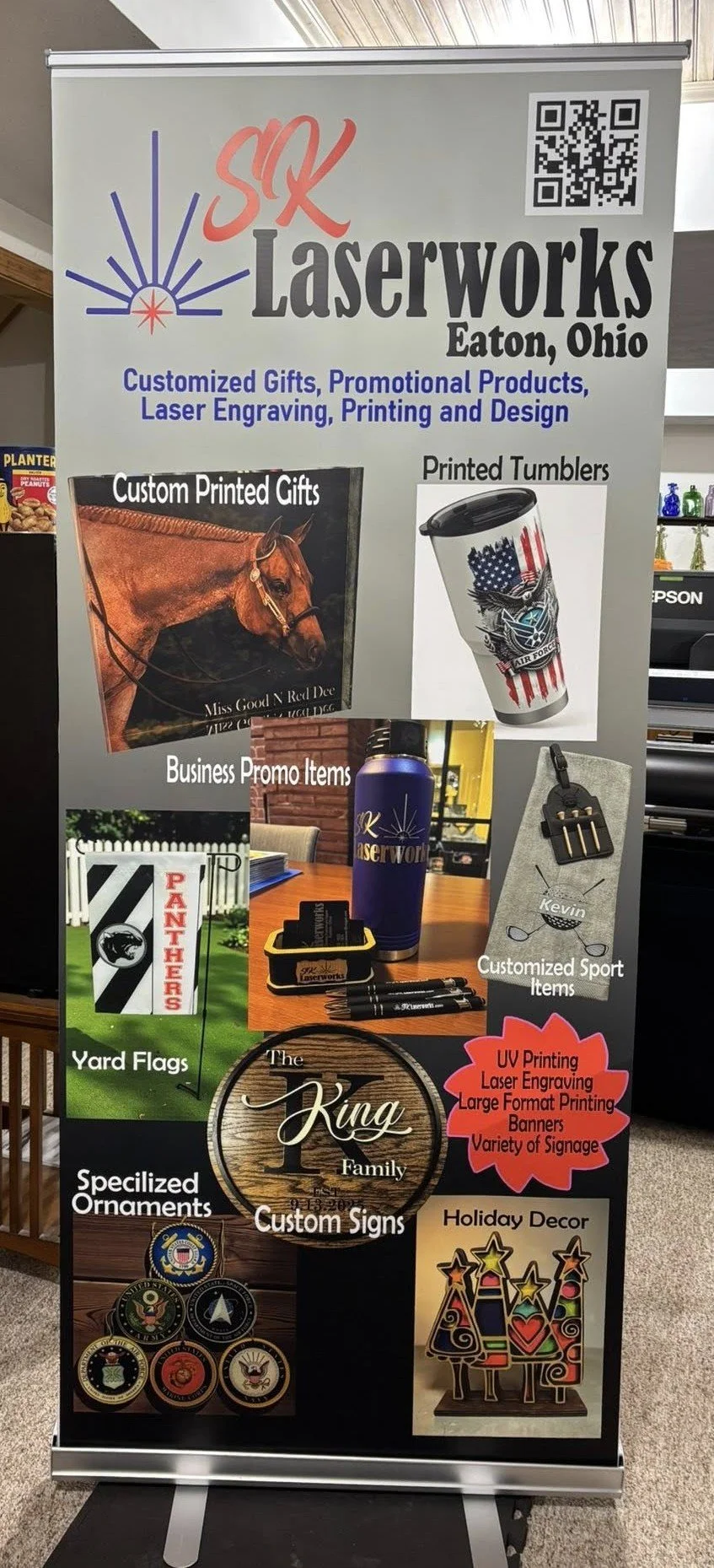 A promotional banner for S&K Laserworks in Eaton, Ohio, advertising customized gifts, promotional products, laser engraving, printing, and design. Features images of printed tumblers, yard flags, custom signs, ornaments, and holiday décor.