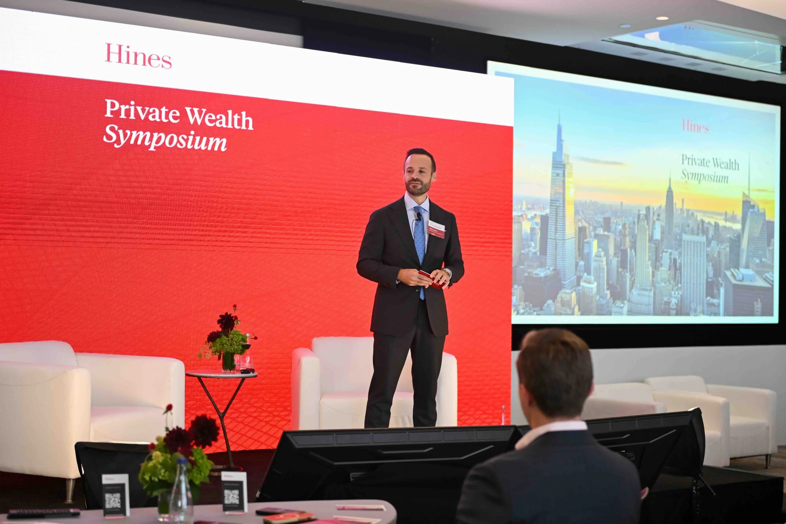 Speaker in a suit presenting in front of a large screen at the Hines symposium