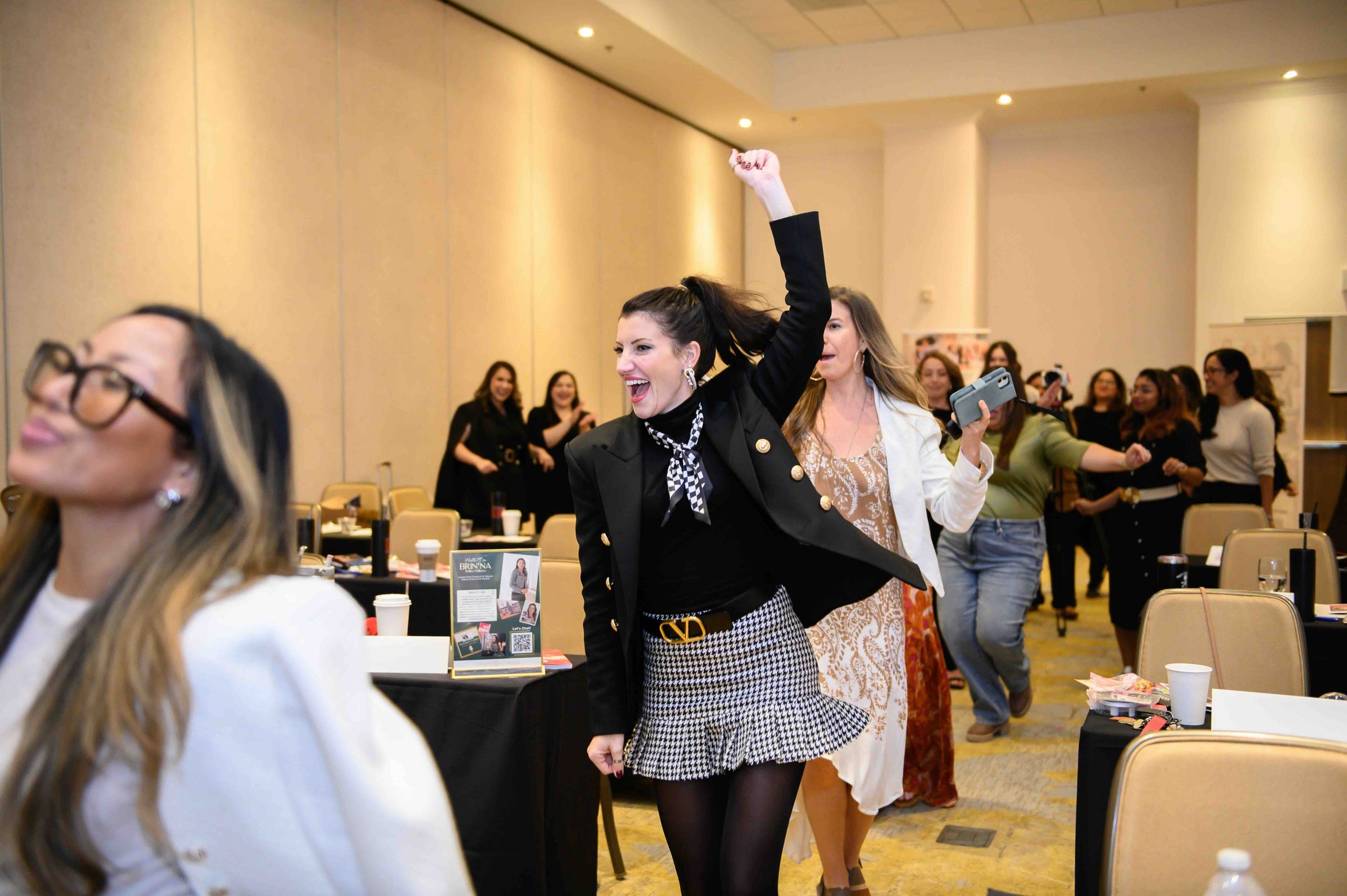 Woman in a black-and-white dress with her arm raised among attendees at tables