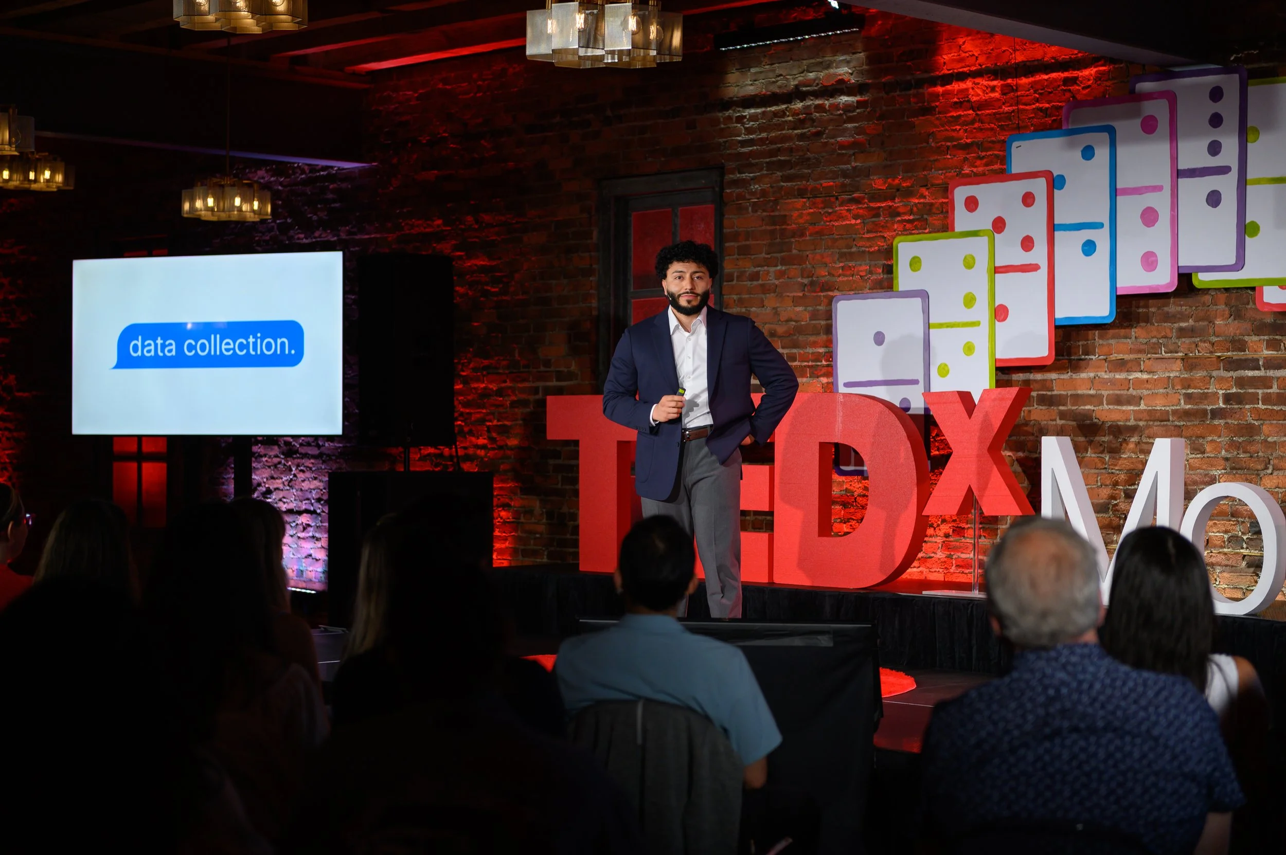 Speaker standing on stage next to a presentation screen at TEDx Montclair
