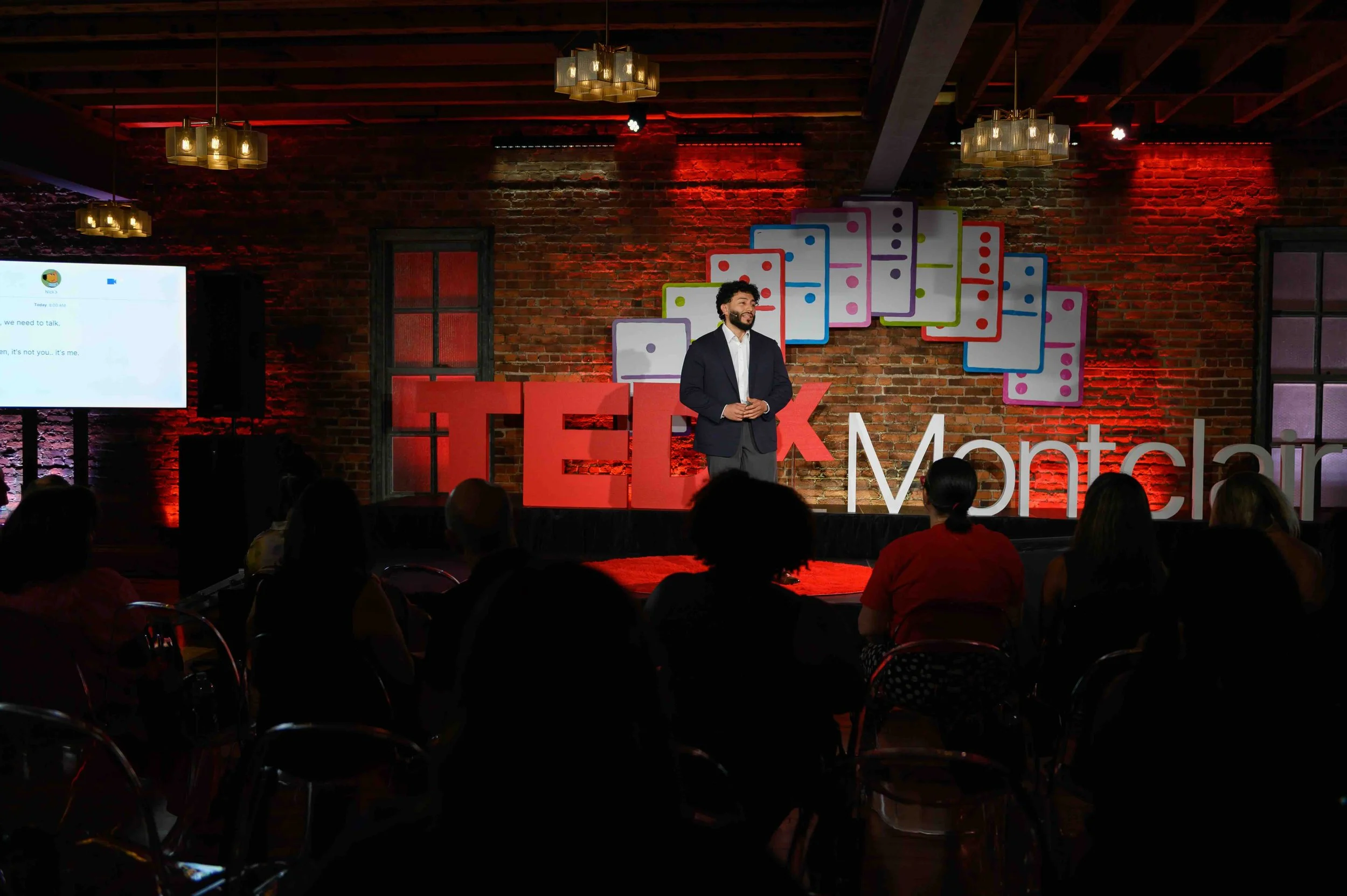 Presenter on the TEDx Montclair stage with a red backdrop
