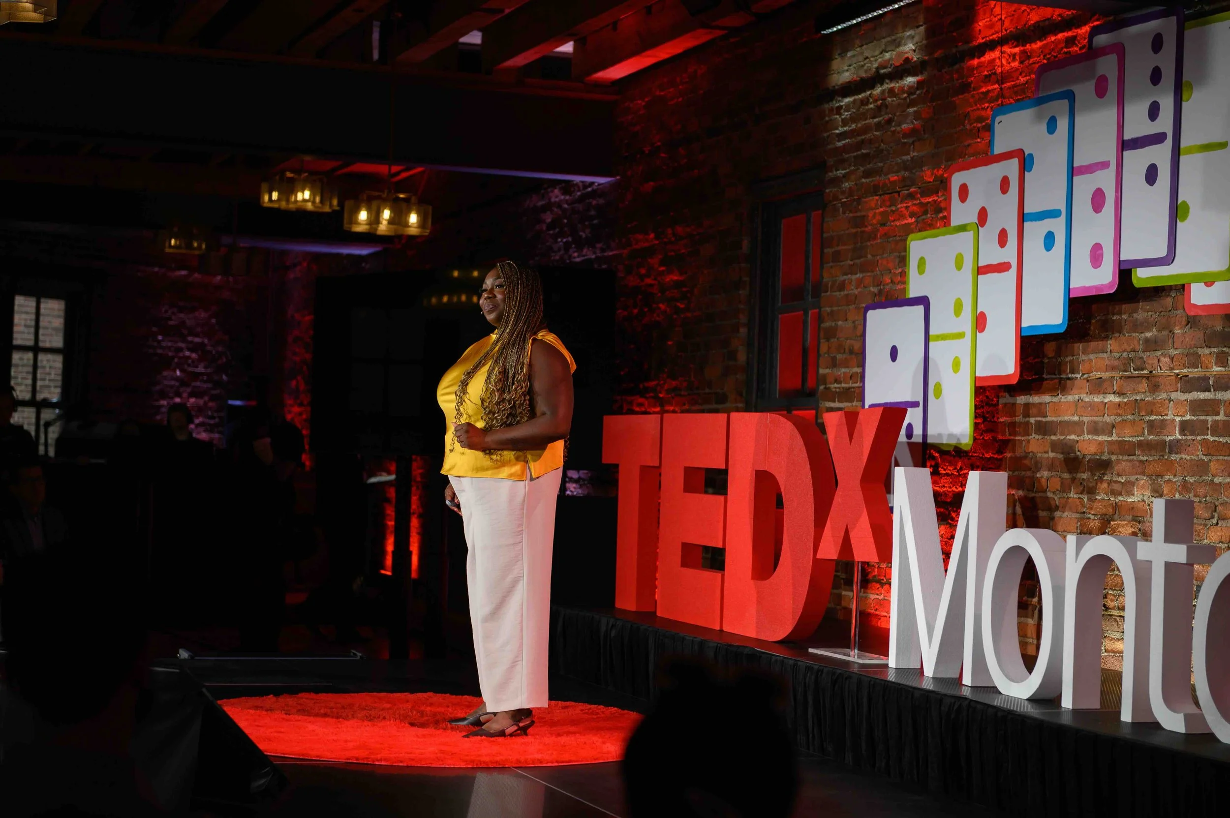 Speaker in a yellow top and white pants standing on the TEDx Montclair stage