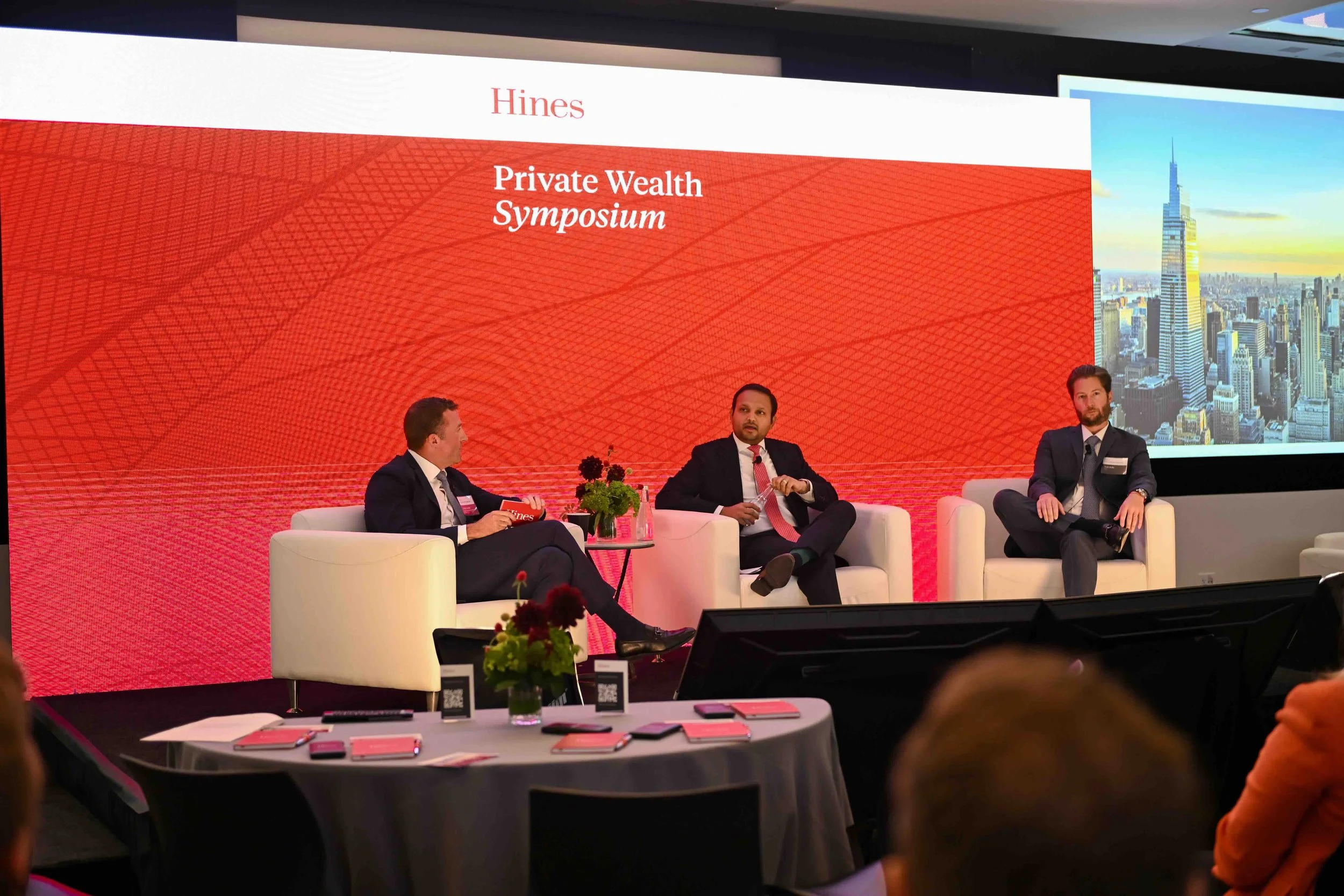 Panel discussion on stage with a red backdrop at the Hines symposium