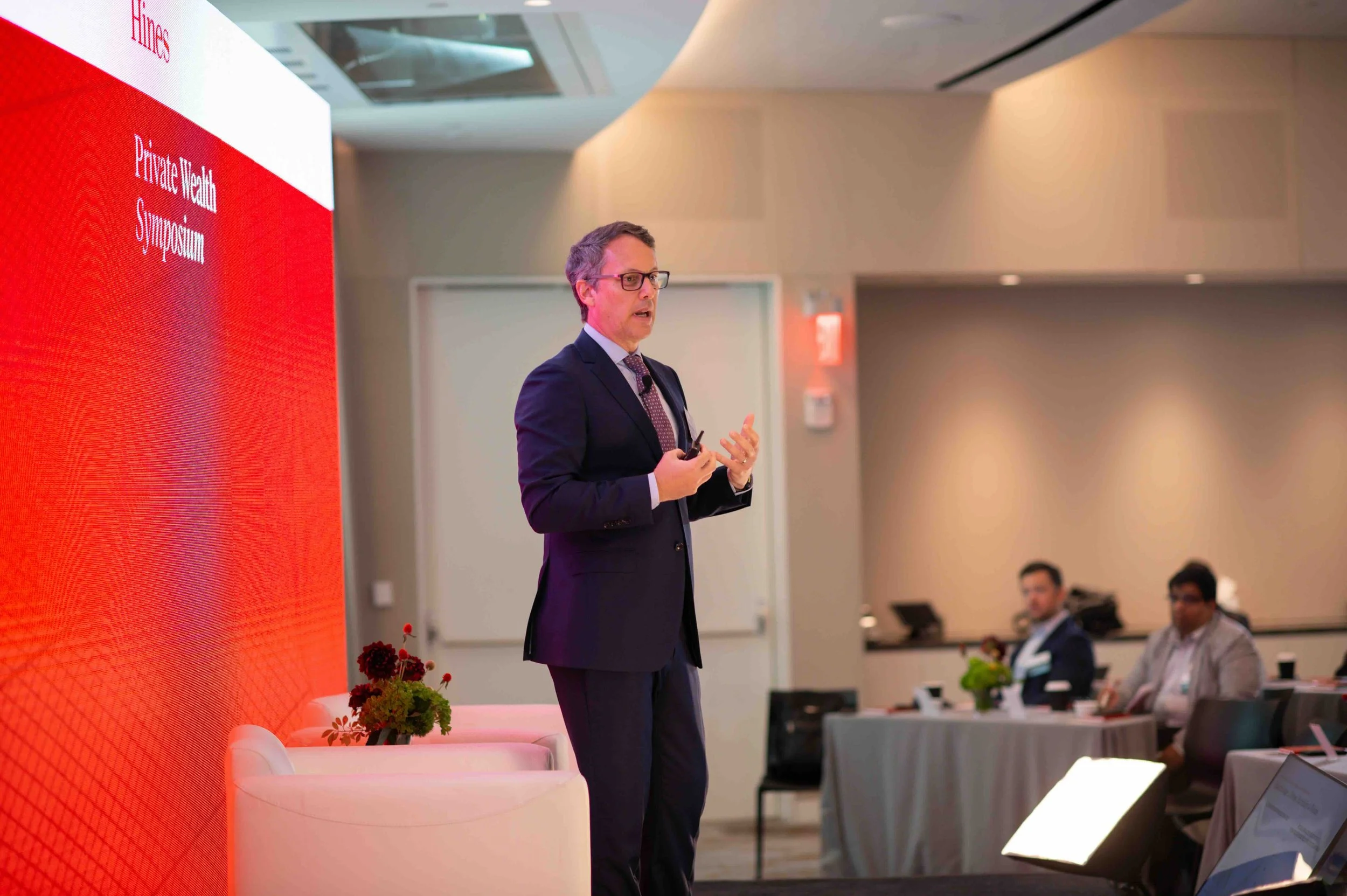Speaker standing and presenting in front of a red wall at the Hines symposium