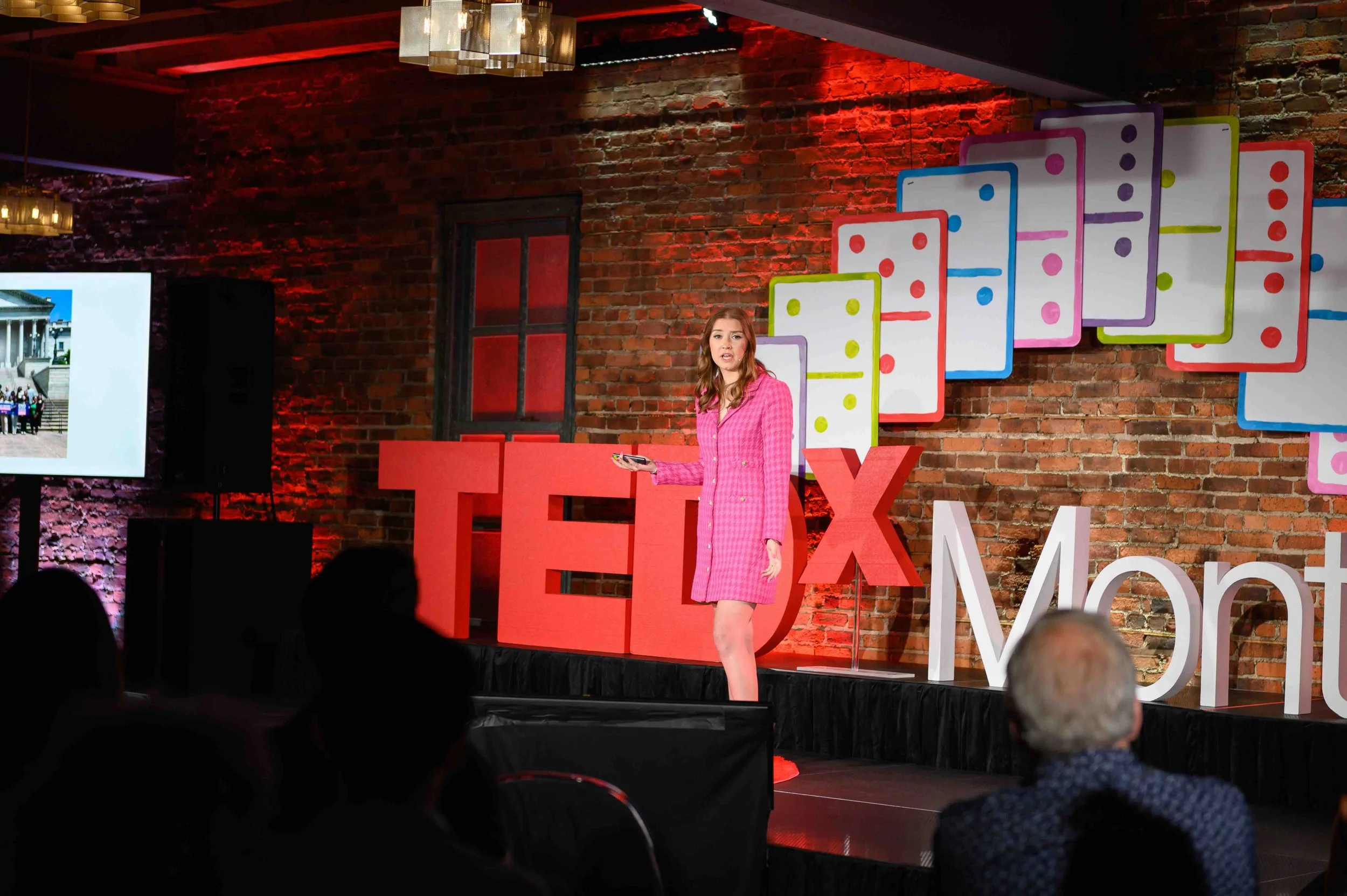 Speaker in a pink outfit on the TEDx Montclair stage with a colorful backdrop behind her