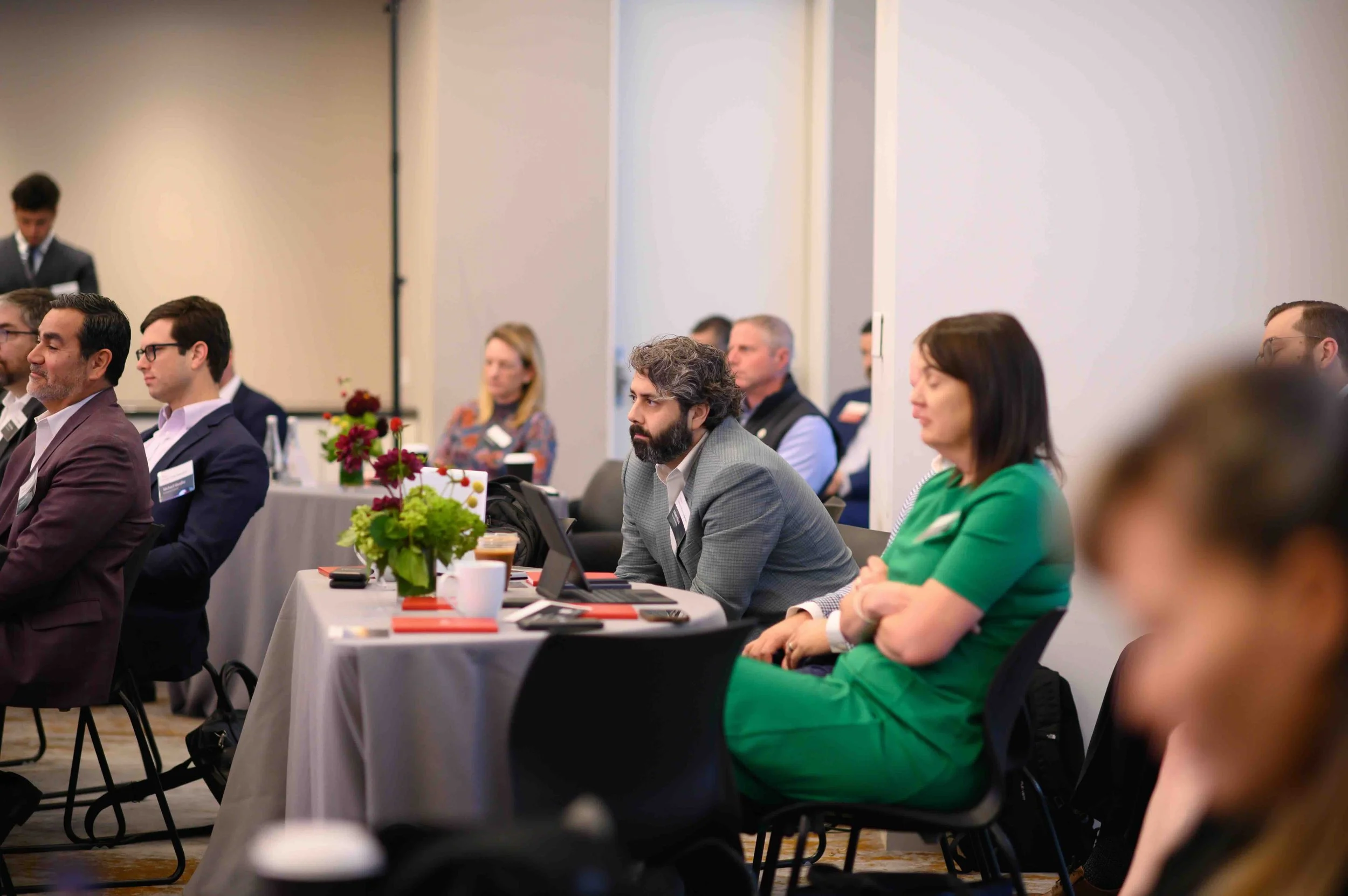 Attendees seated at a round table, including a woman in a green dress, at the Hines symposium