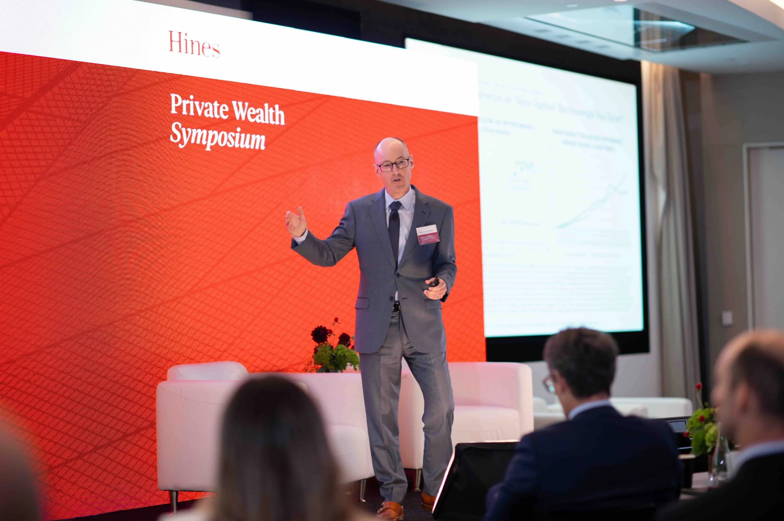 Speaker presenting in front of a screen at the Hines Private Wealth Symposium