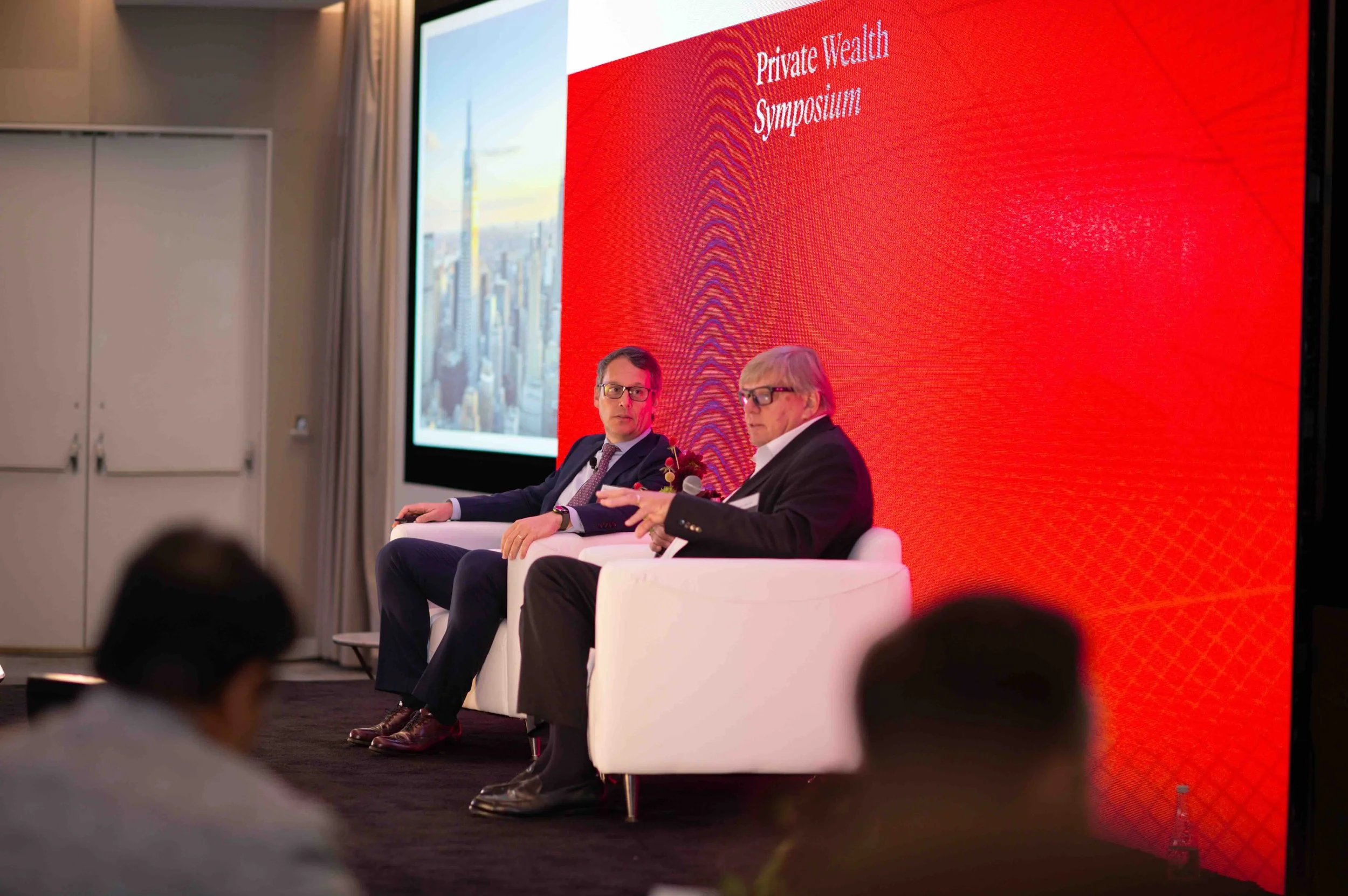 Panel of speakers seated on stage in front of a red screen at the Hines symposium