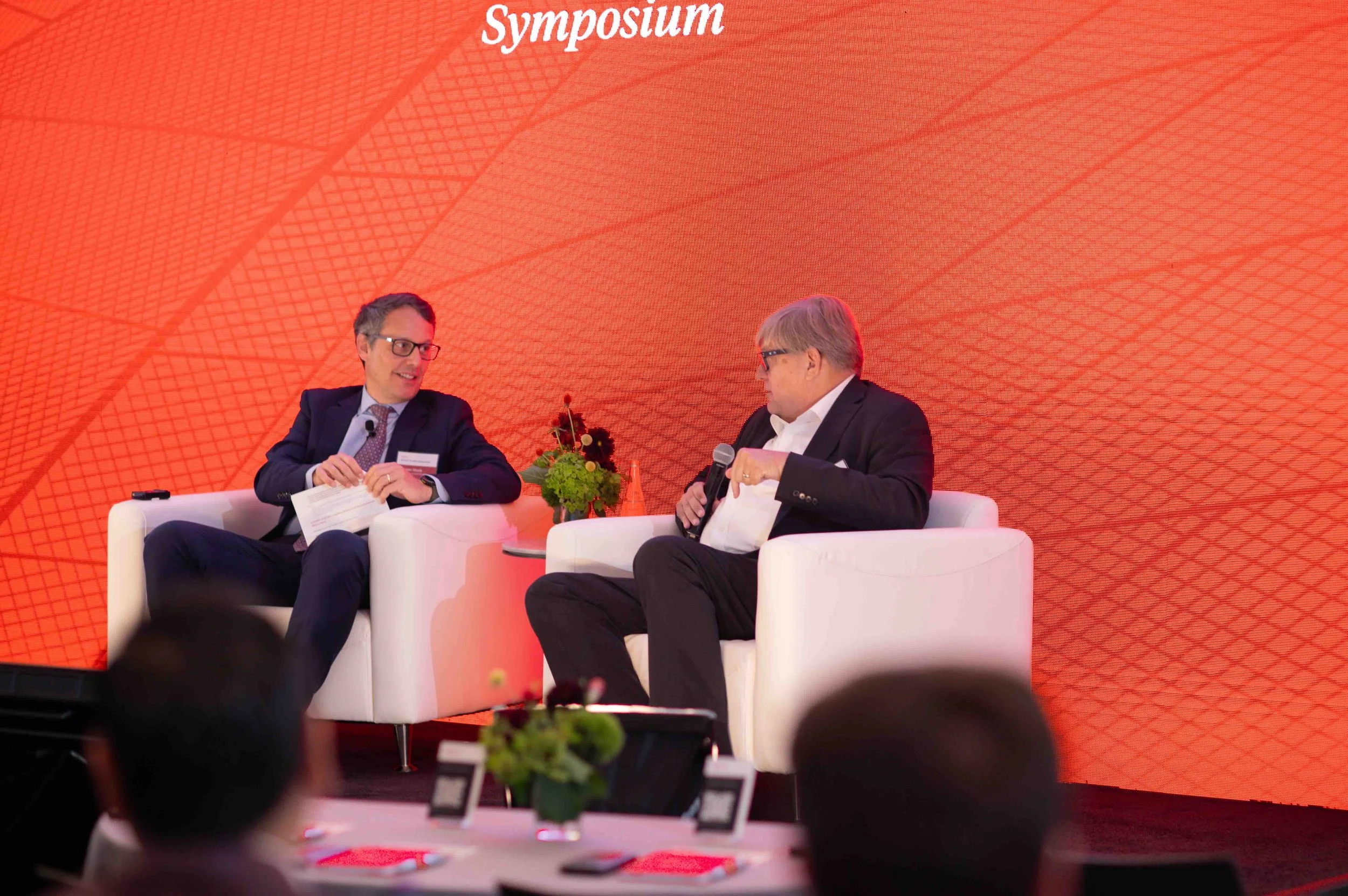 Two speakers seated in white chairs on stage at the Hines symposium