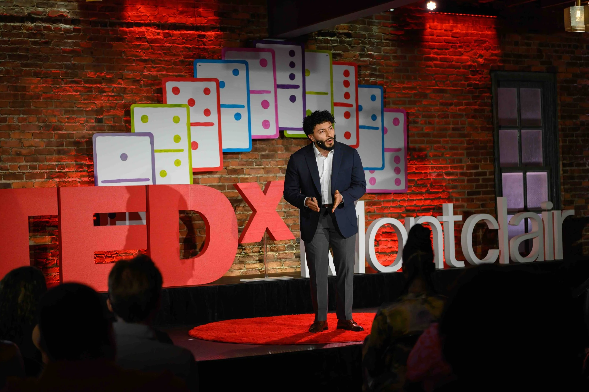 Speaker in dark clothing on the TEDx Montclair stage under red lighting