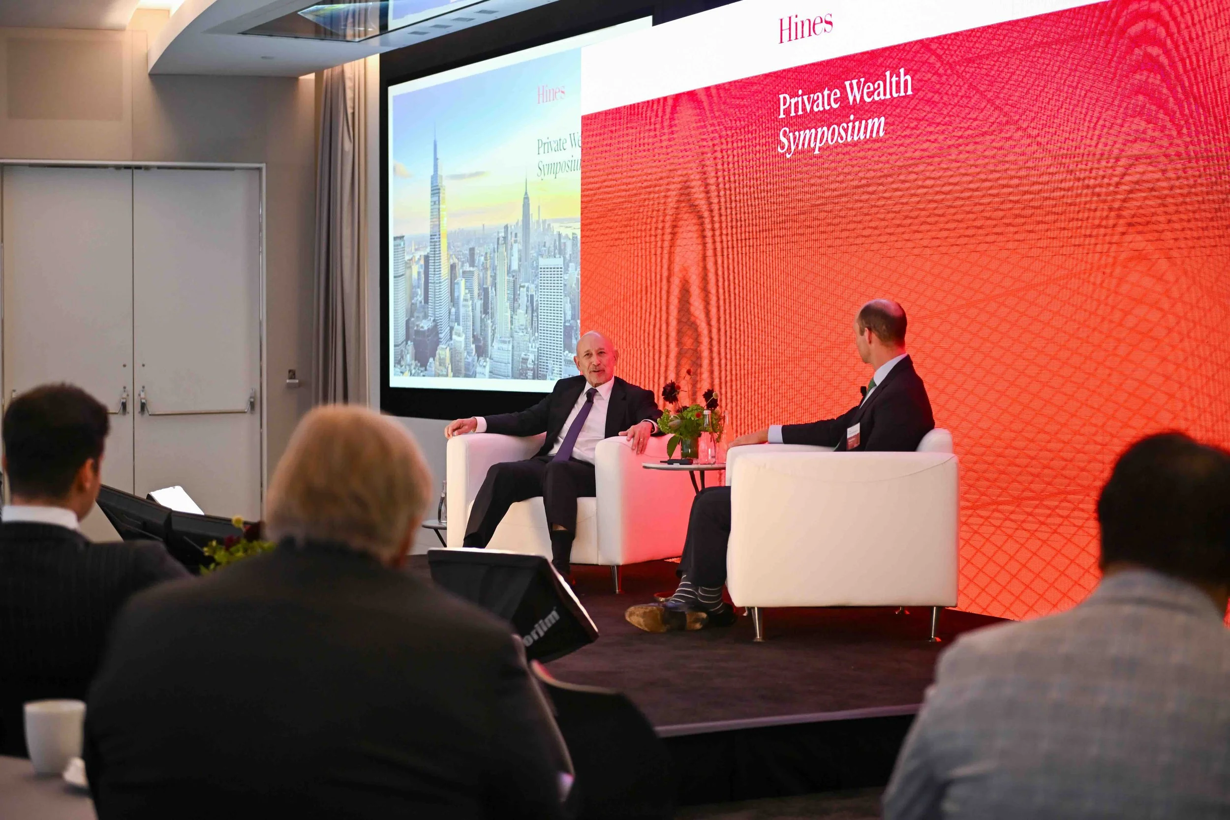 Panelists seated on stage in front of a screen at the Hines symposium