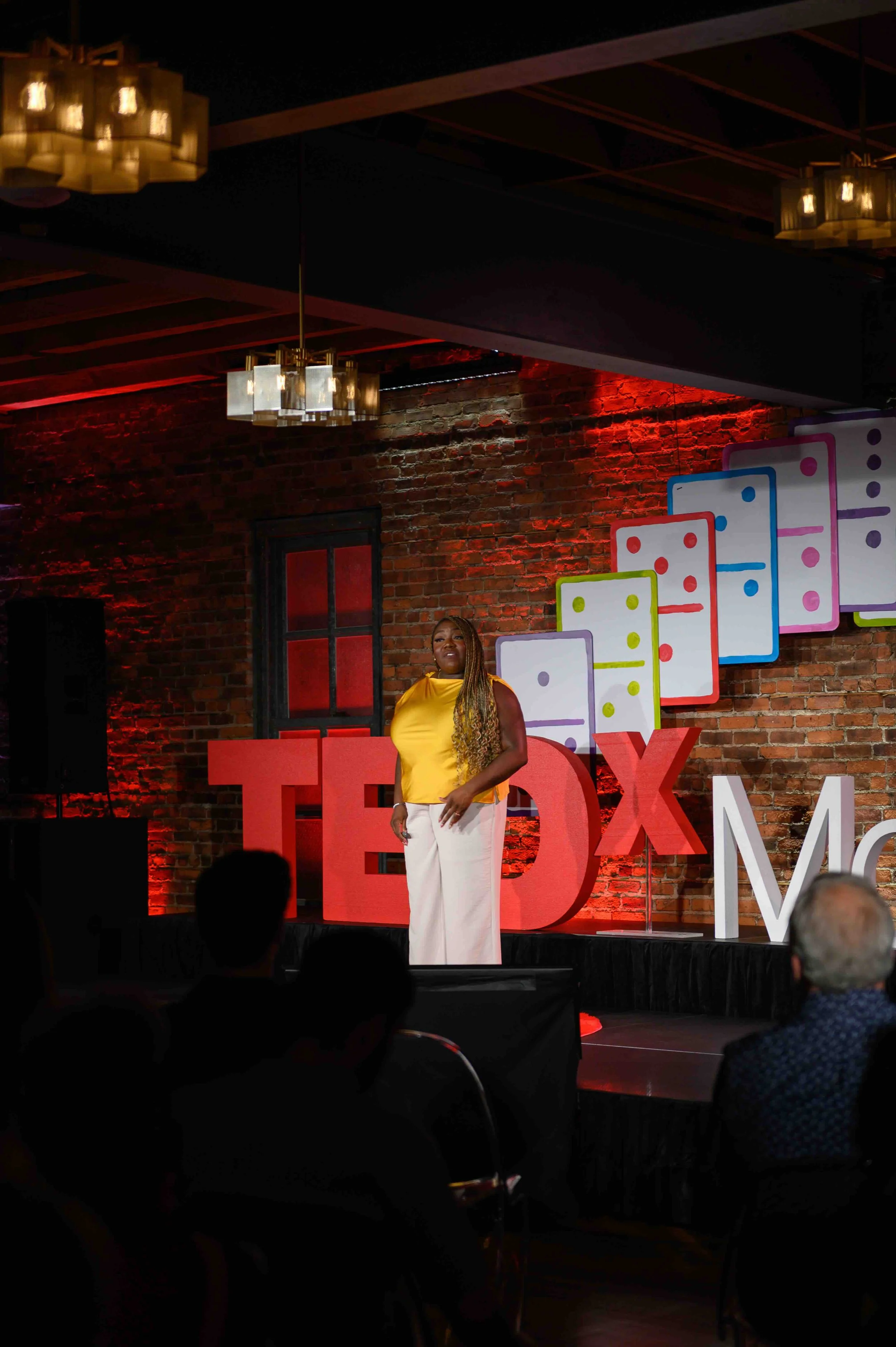 Speaker standing on the TEDx Montclair stage under warm red lighting