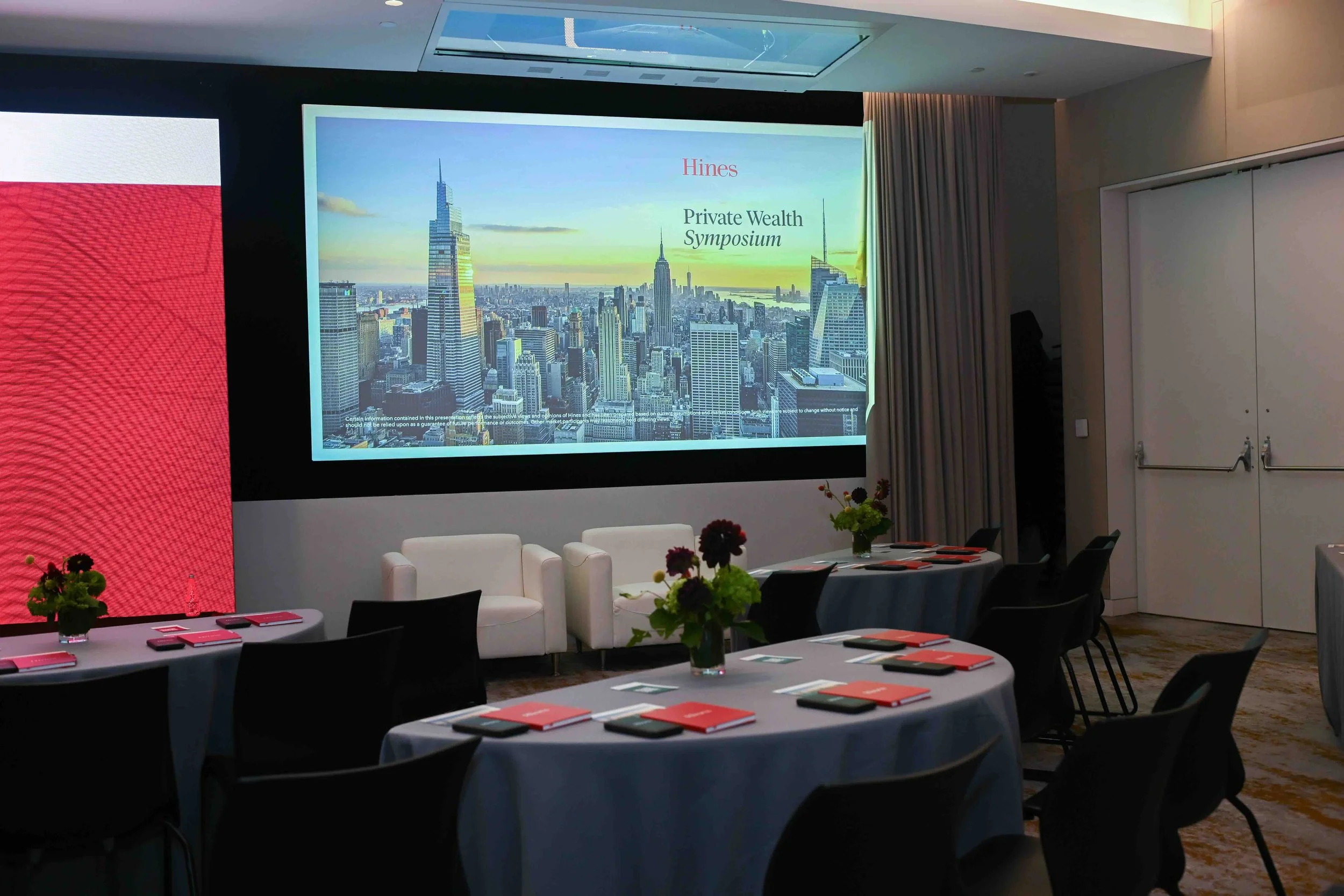 Conference room set with round tables and a presentation screen before the Hines symposium