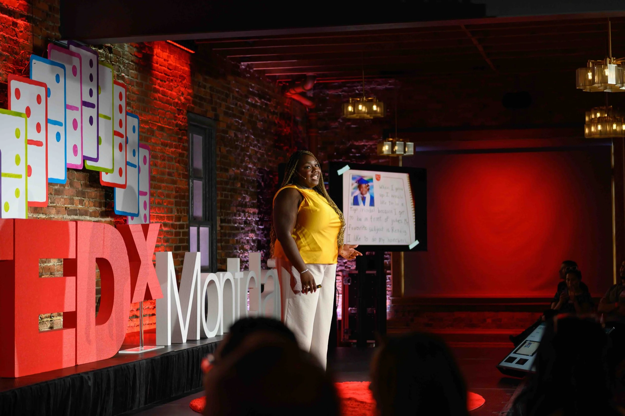 Speaker in a yellow top standing on the TEDx Montclair stage beside a whiteboard