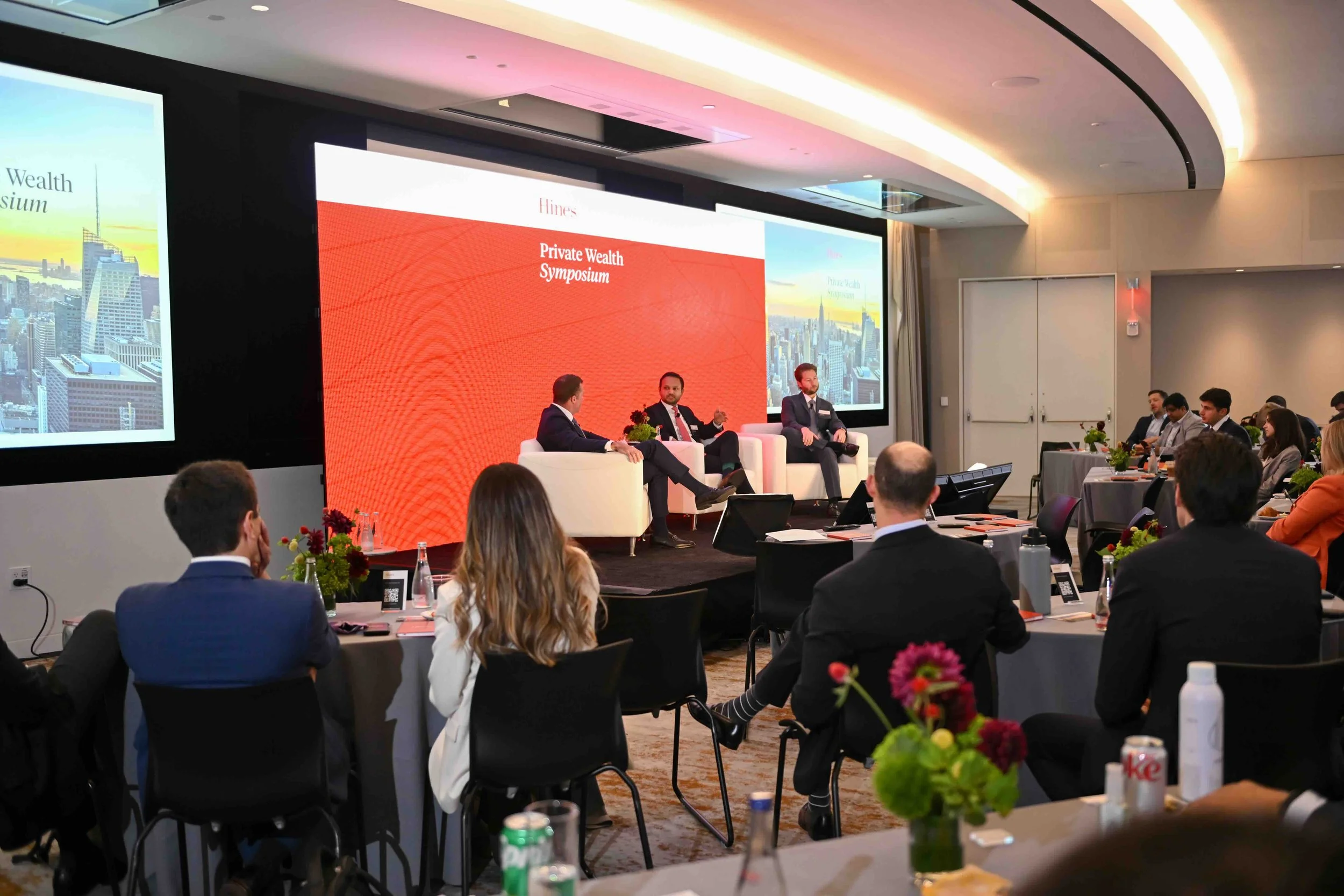 Wide view of the ballroom with attendees and a red presentation screen at the Hines symposium