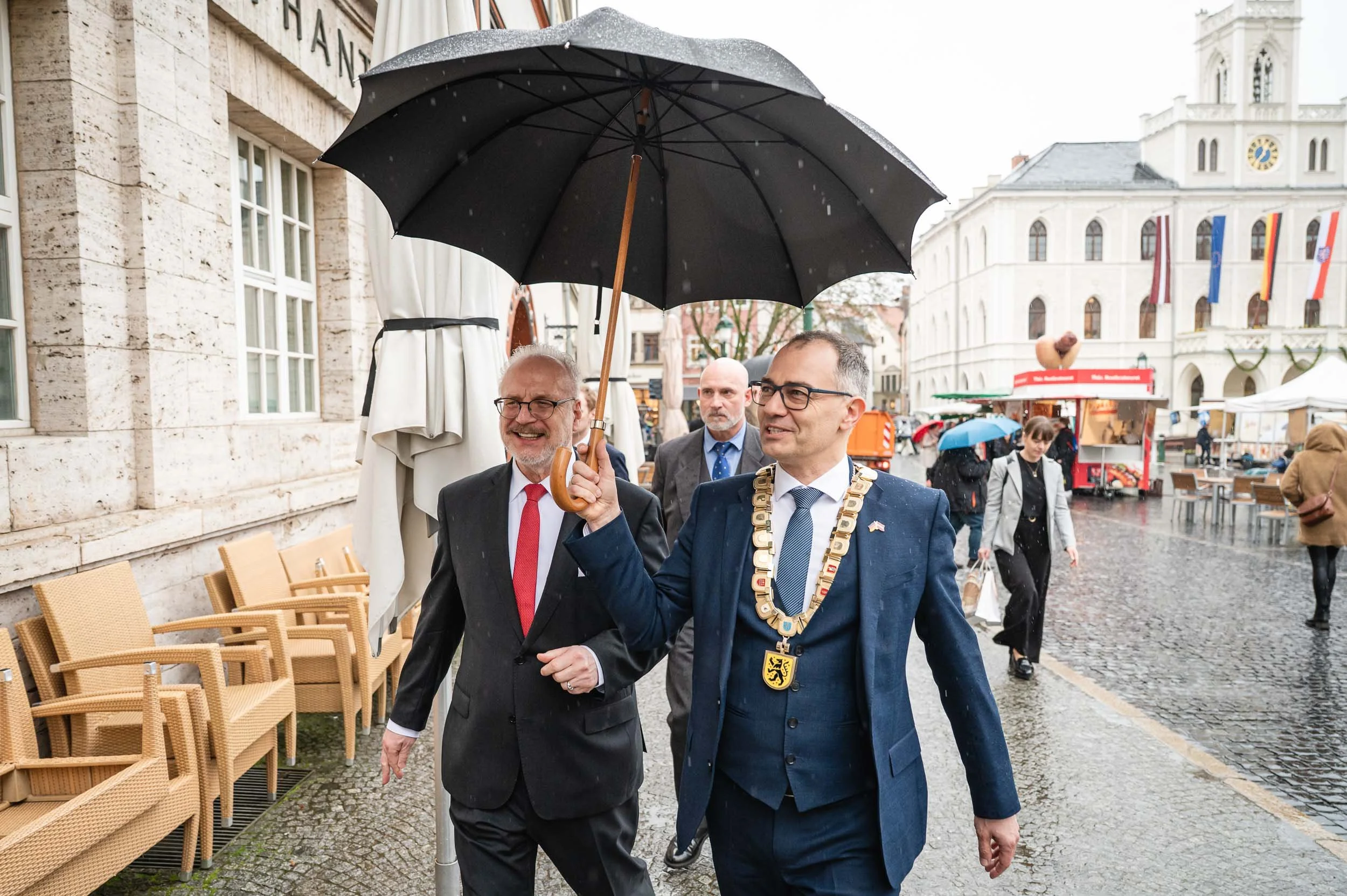 Zwei Männer in Anzügen mit Regenschirm in der Weimarer Altstadt, einer mit Amtskette. Veranstaltungsfotografie.