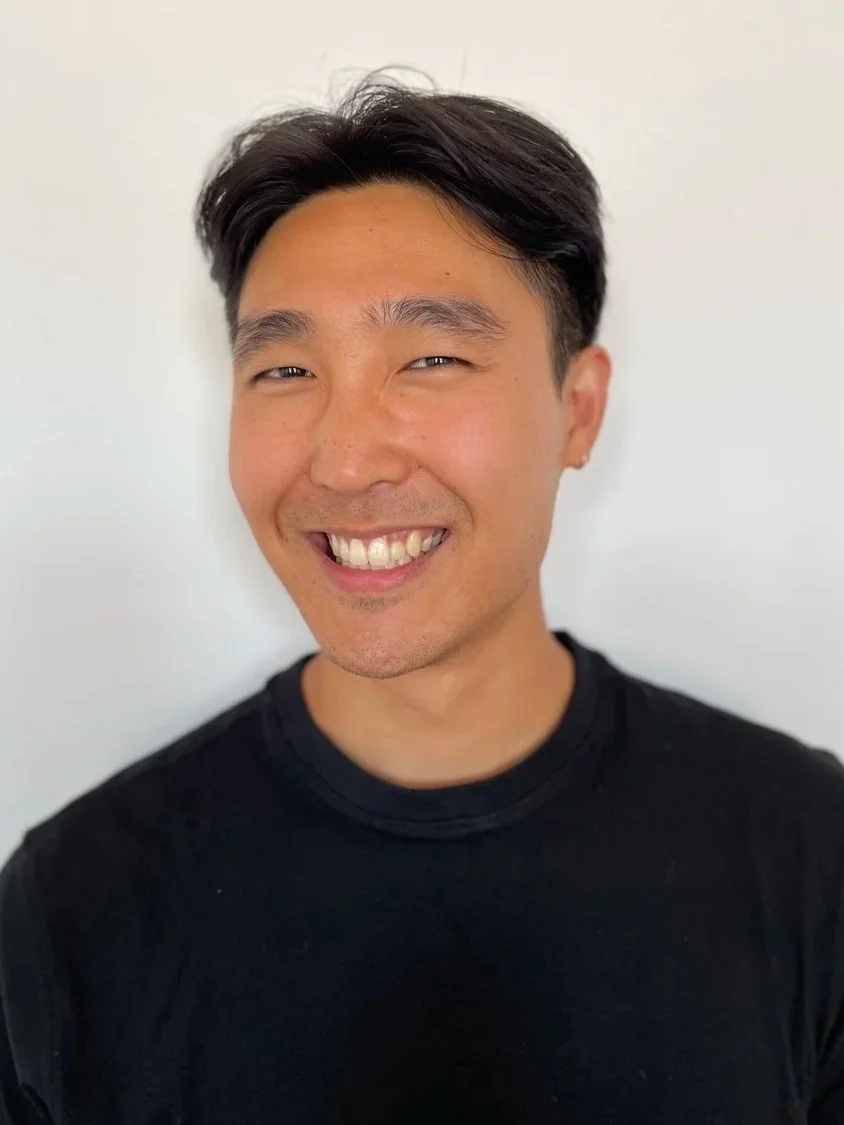 Smiling man with short dark hair wearing a black shirt against a plain white background.