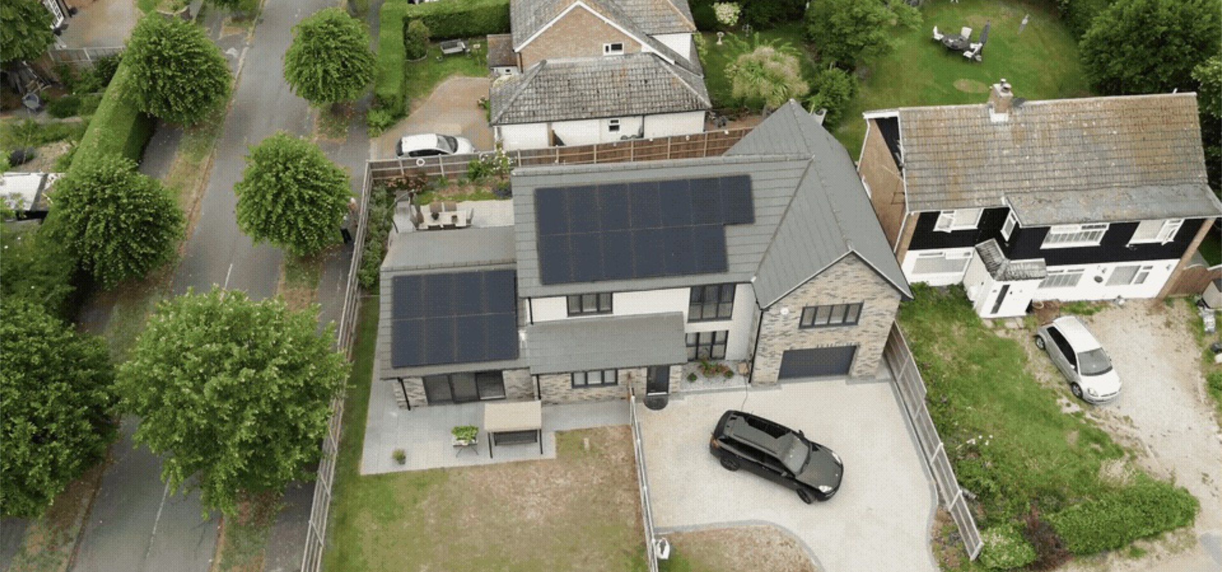 Aerial view of a suburban house with rooftop solar panels, a private driveway, and green residential gardens.