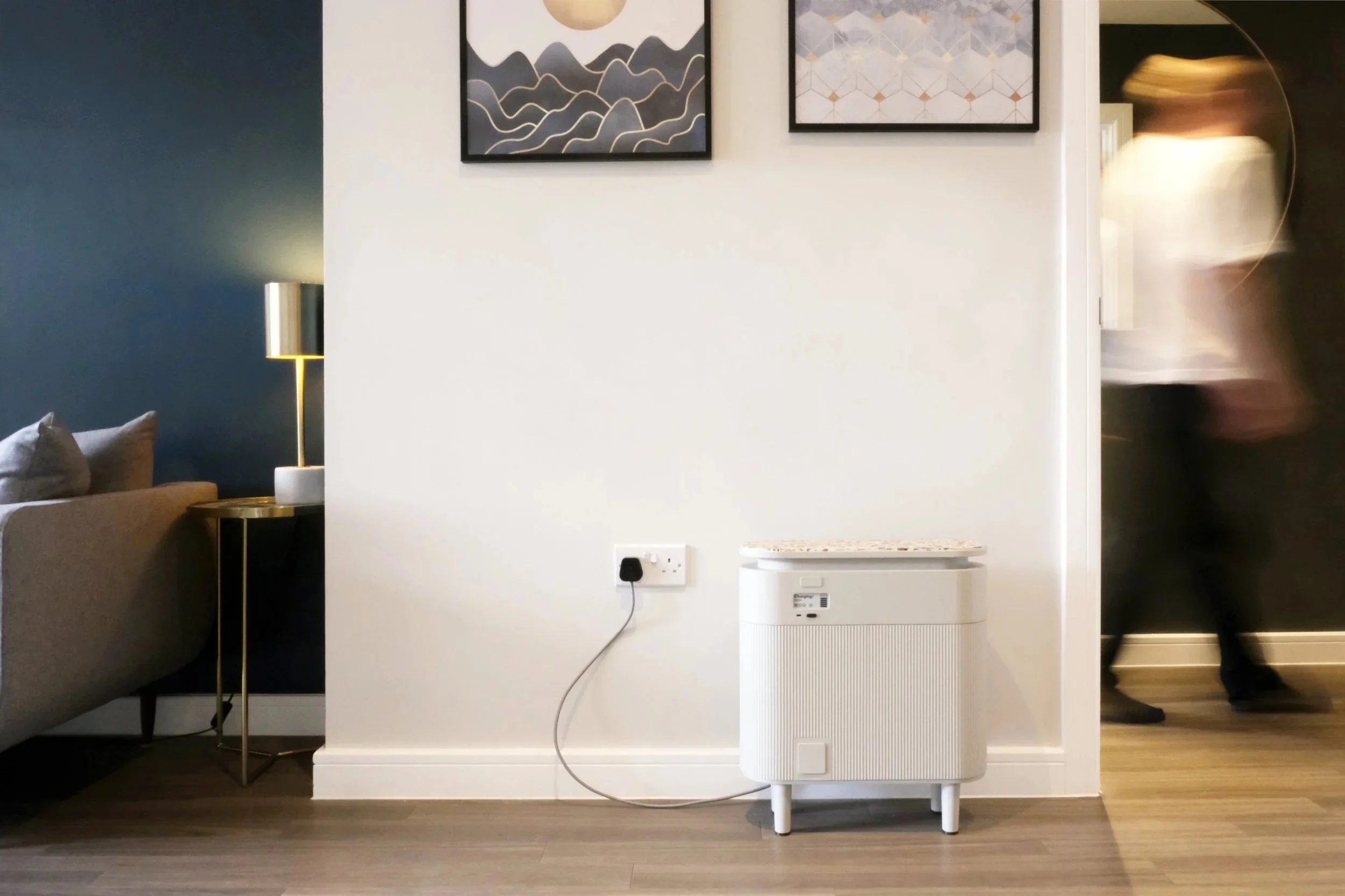 Windfall Battery plugged into a plain white wall as a flat tenant walks past in the background.
