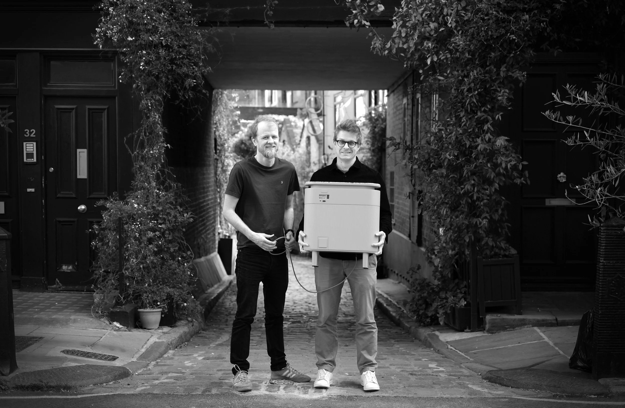 Founders Ashley and Rob holding the Windfall home battery in a black and white outdoor photograph.
