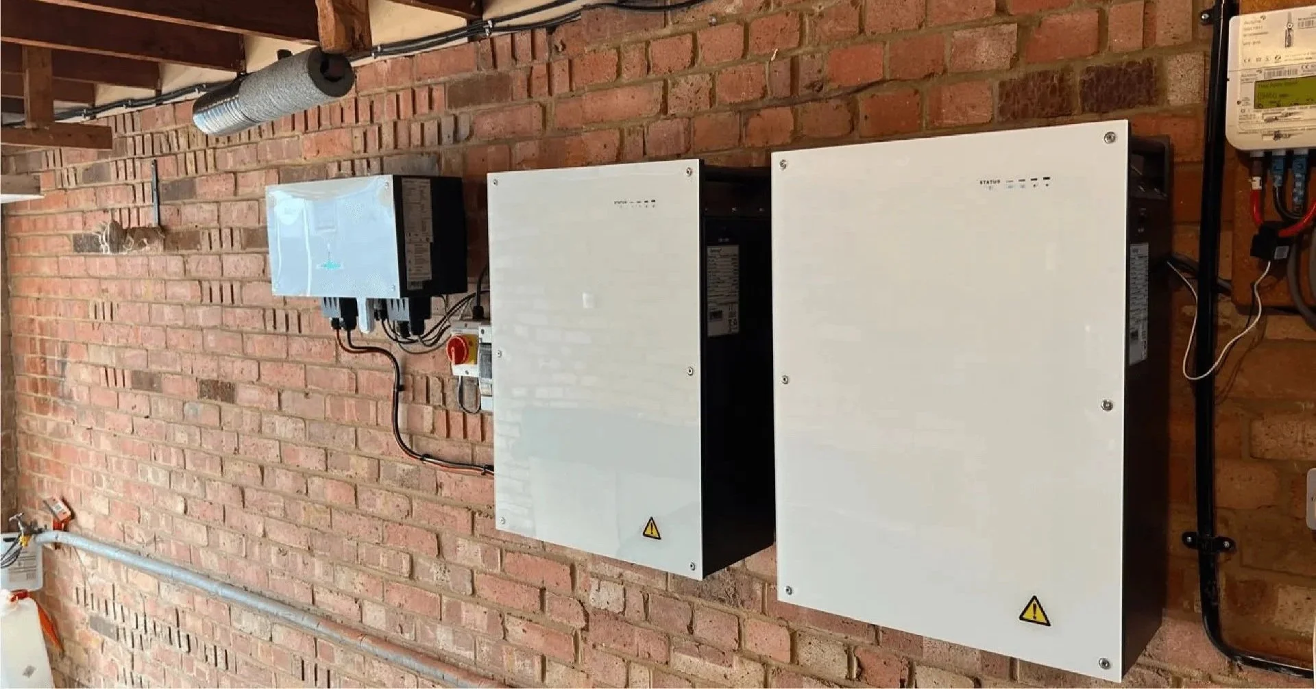 Traditional home battery storage unit mounted on a brick wall with exposed wiring installation.